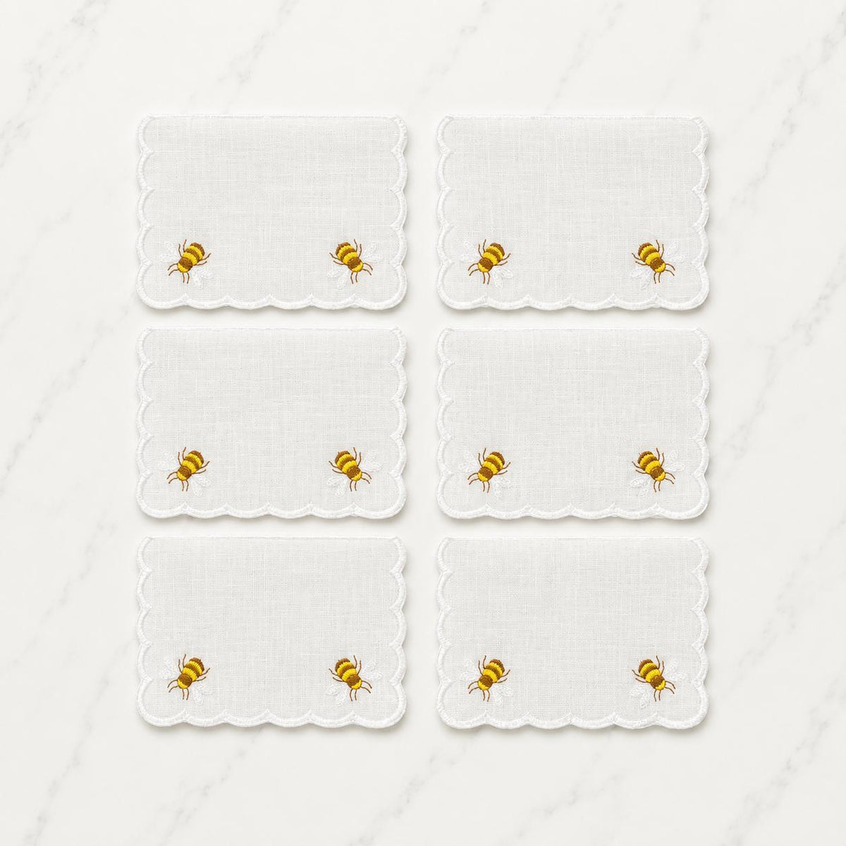 Six white cocktail napkins with scalloped edges and two embroidered honey bees each