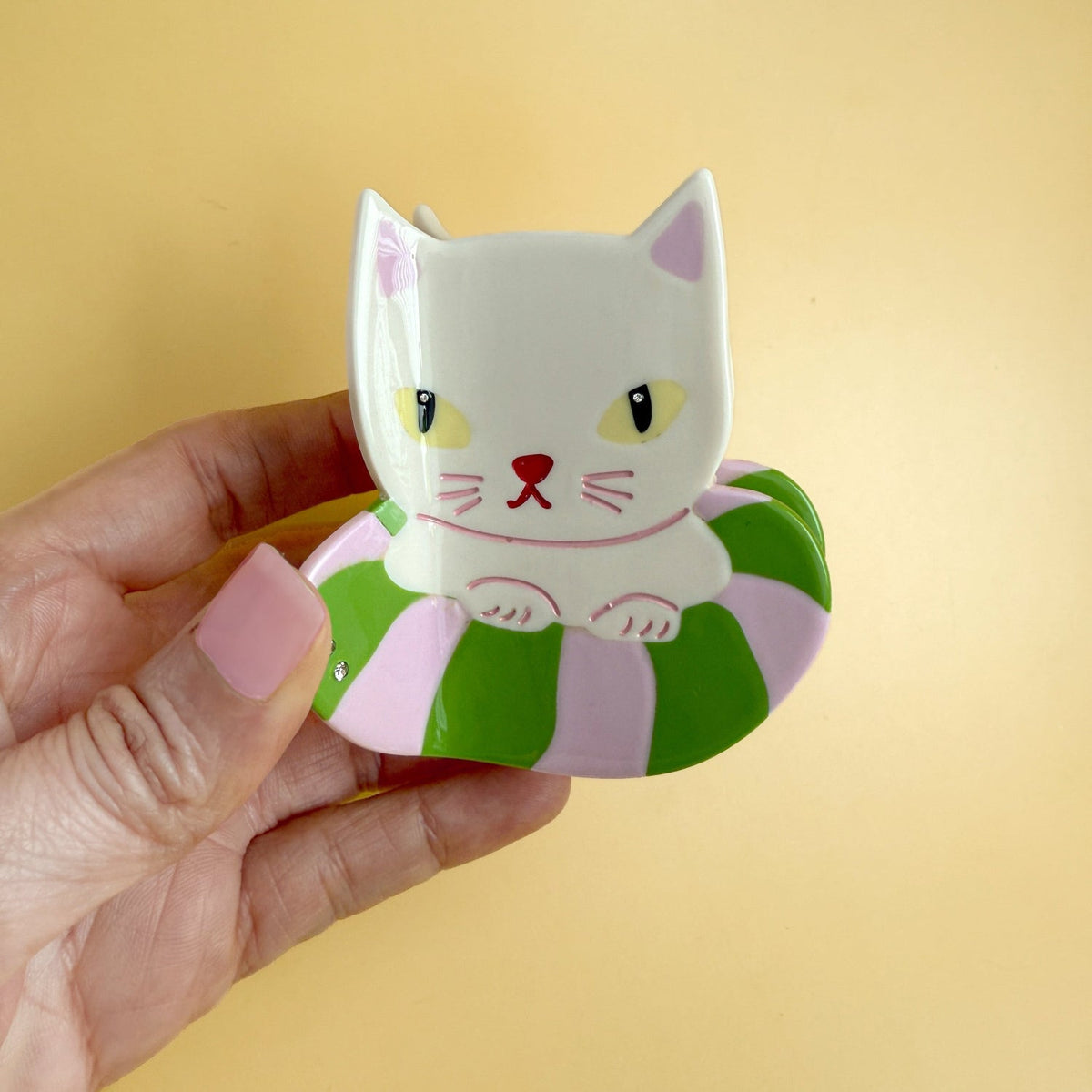 Cat hair claw clip held in hand, white cat face with green-and-pink swirls