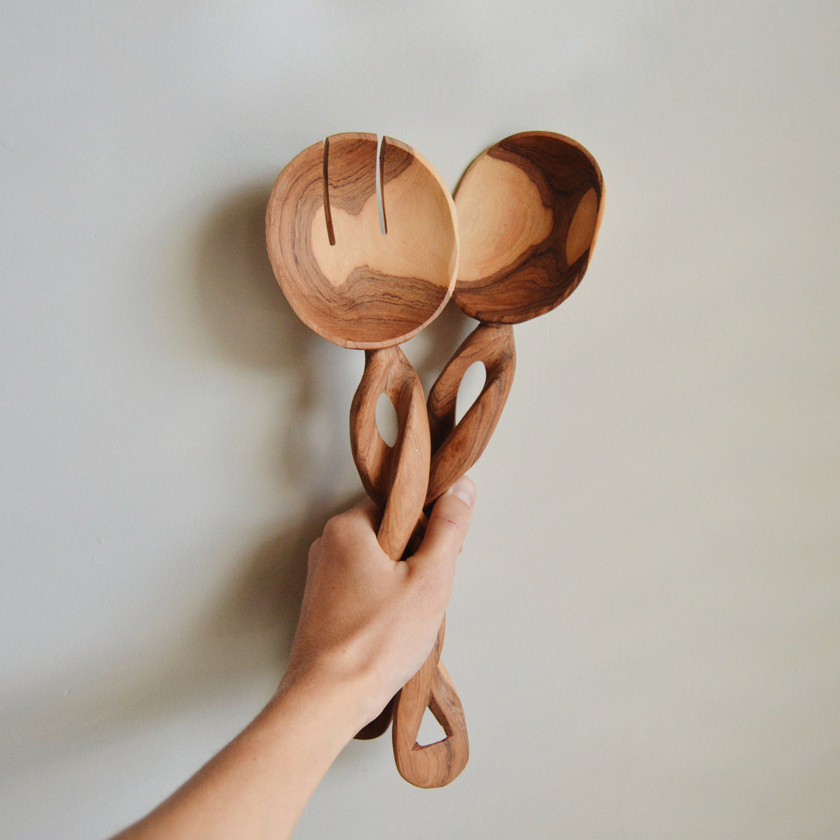 Olive wood spiral serving spoons with round scoops and carved oval cutouts (pair), held.