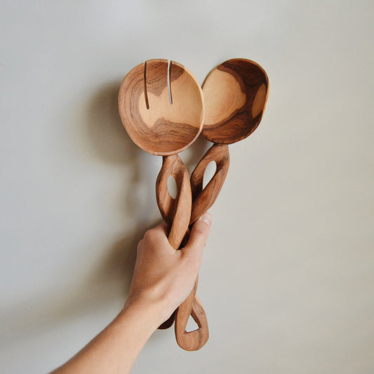 Olive wood spiral serving spoons with round scoops and carved oval cutouts (pair), held.
