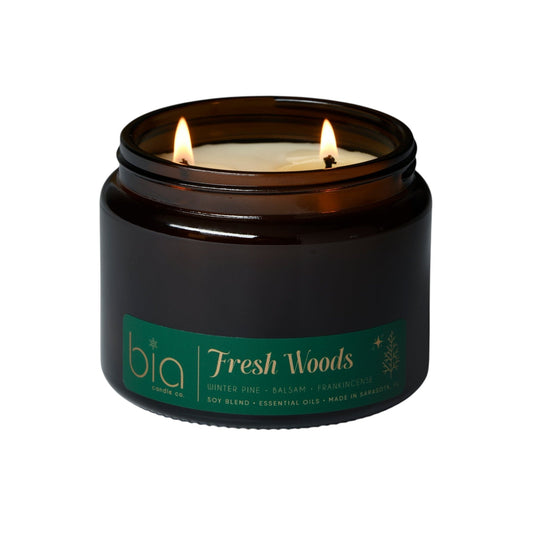 Black glass candle jar with lit wick and green label, Fresh Woods