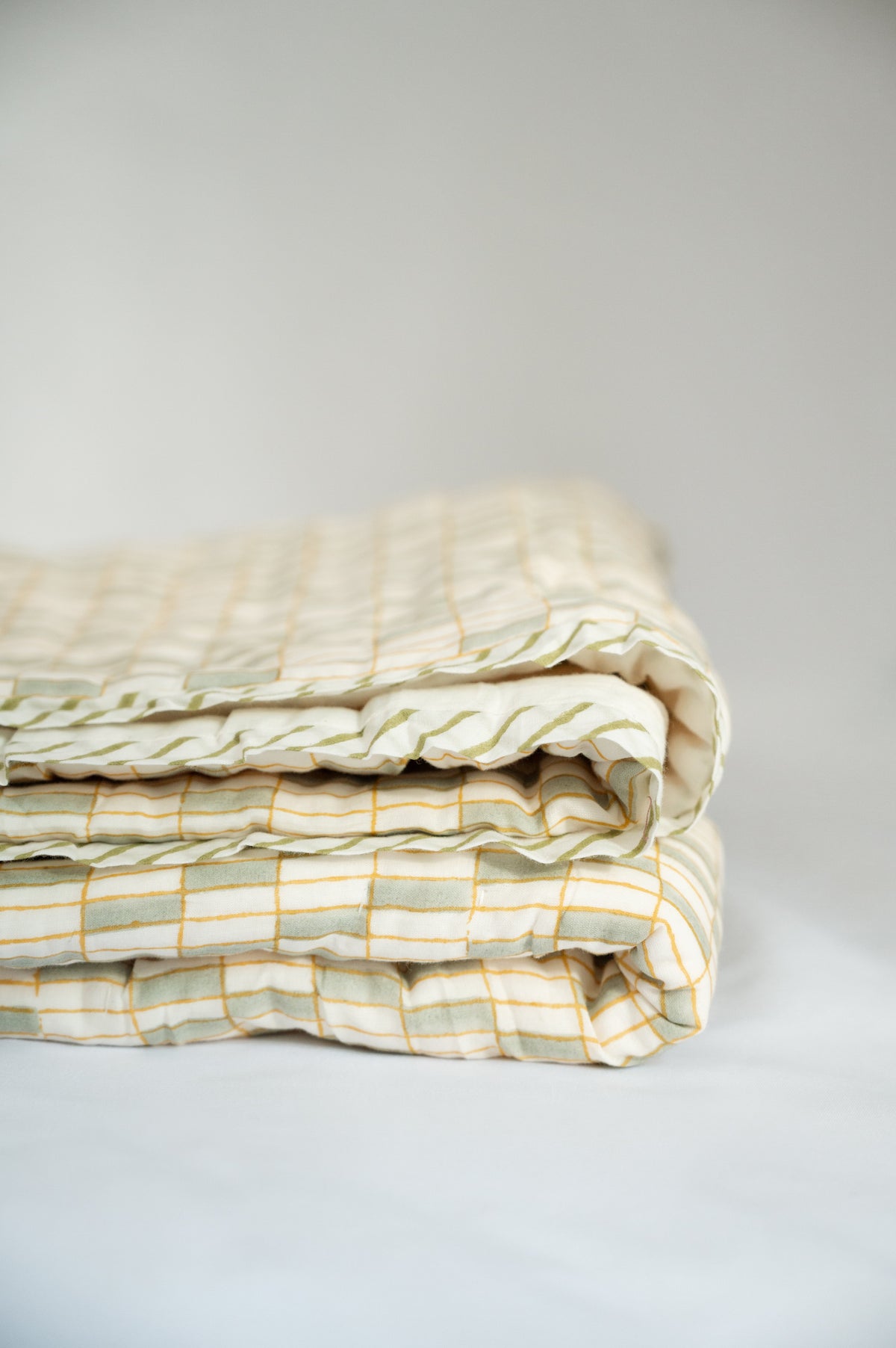 Folded quilt stack in green, white, and yellow with crisscross plaid quilting lines