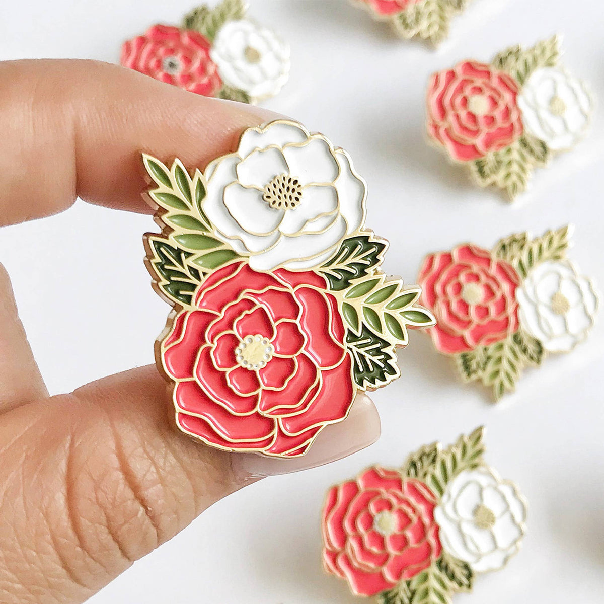 Floral enamel lapel pin with red and white flowers, green leaves, and gold outline