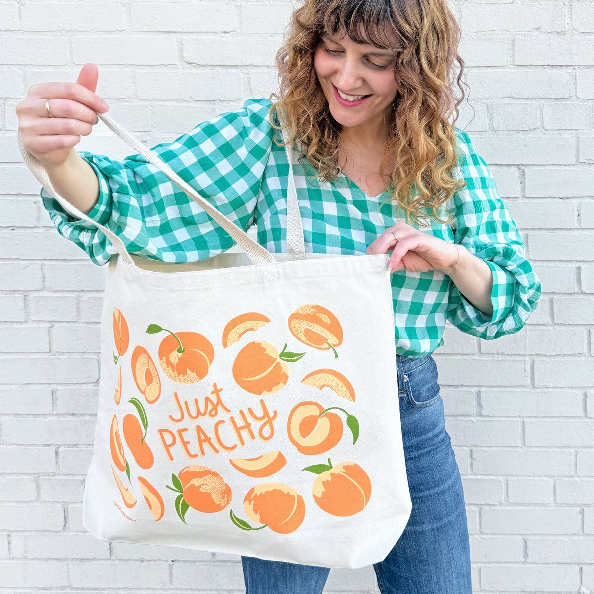 Canvas tote bag with orange fruit graphics and “Just Peachy” message, worn on shoulder