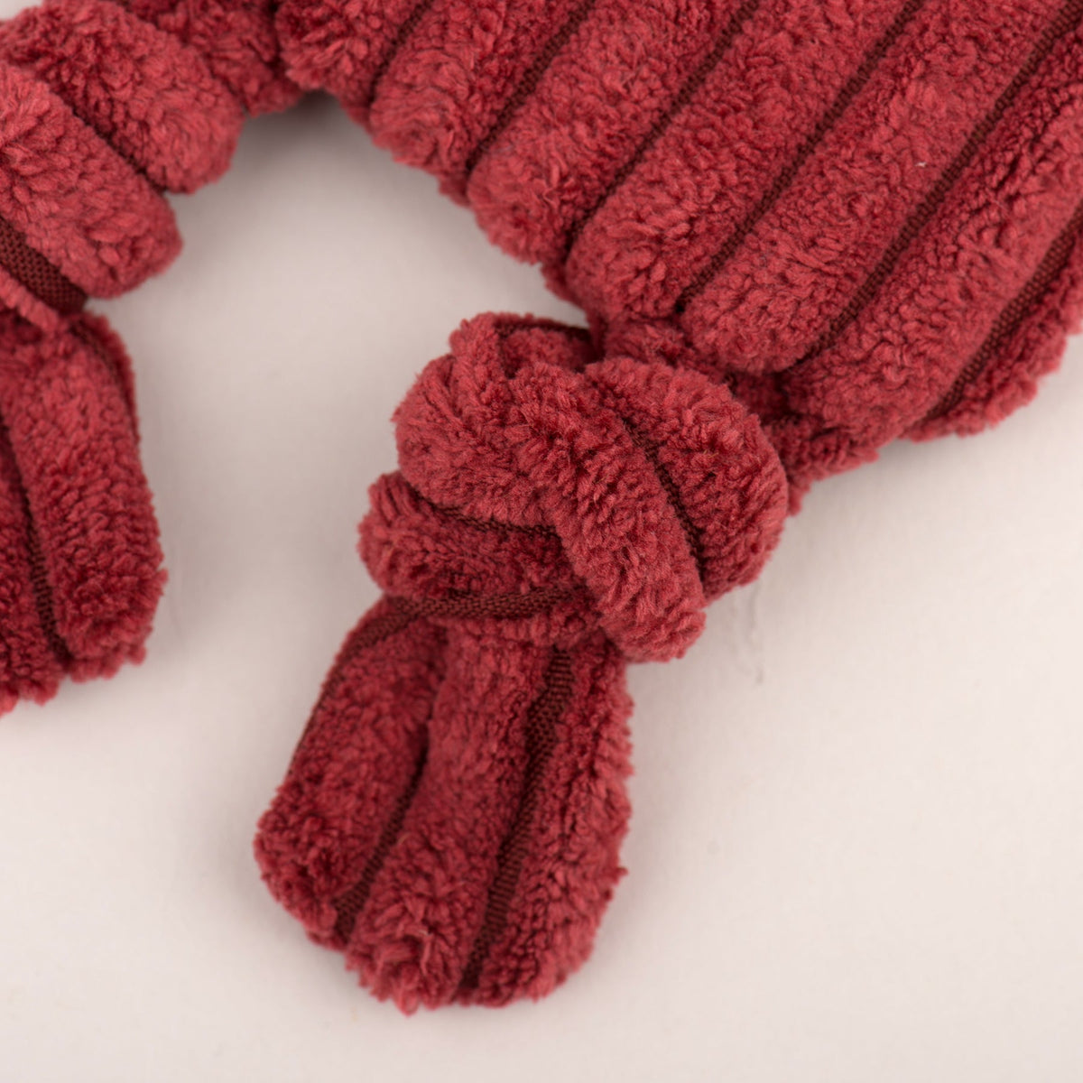 Close-up of red plush fox toy's knotted leg and ribbed body