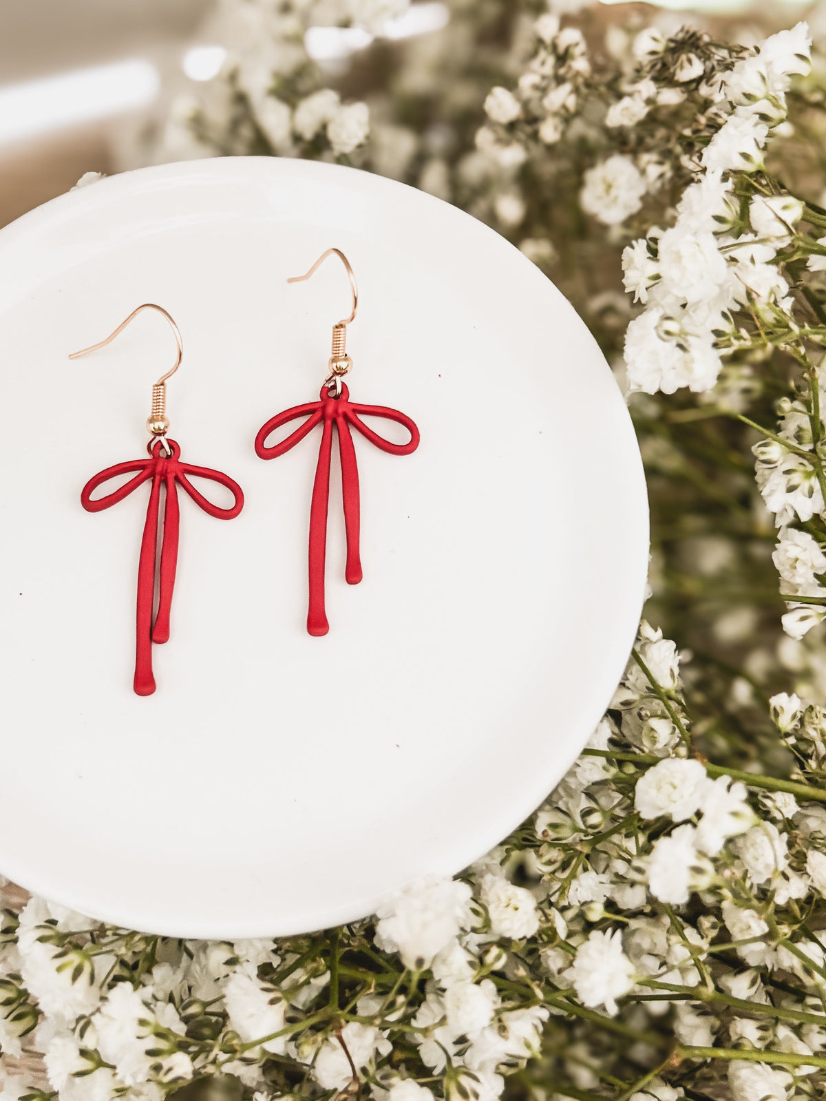 Red bow drop earrings with tassel drops and gold-tone hooks, on a white display plate