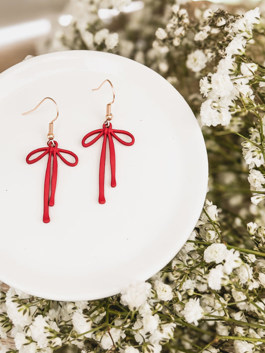 Red bow drop earrings with tassel drops and gold-tone hooks, on a white display plate