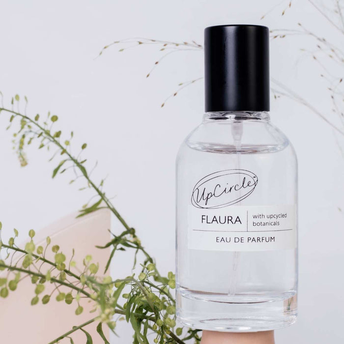 Flaura eau de parfum bottle with black cap and clear label, with green stems nearby.