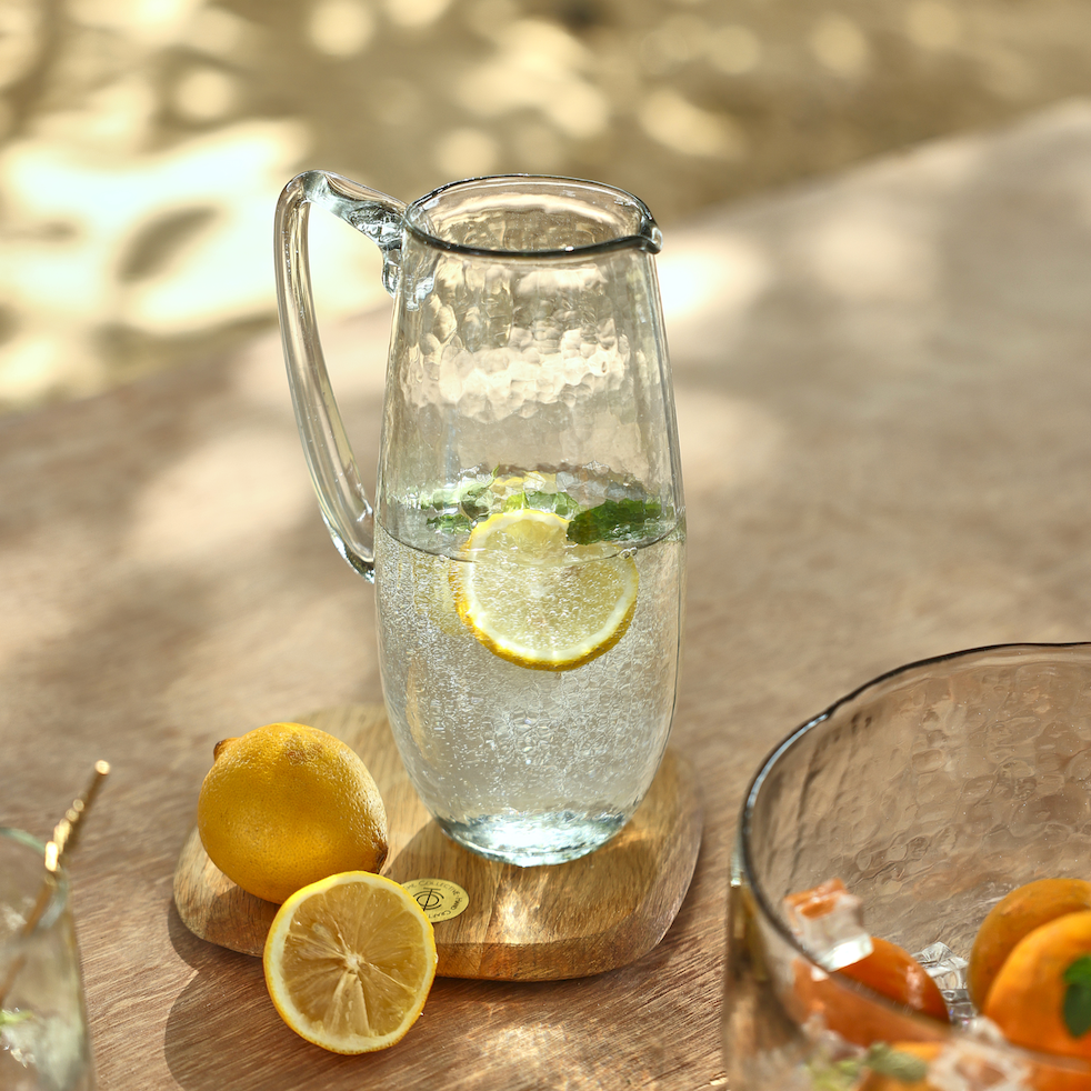 Glass pitcher with pebbled texture, clear citrus water with lemon slices and green garnish