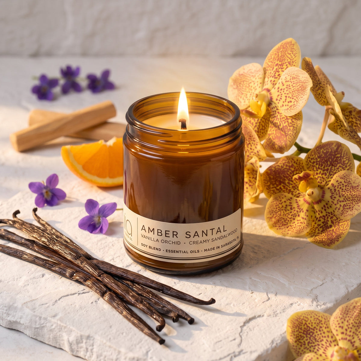 Close-up amber candle jar with lit wick and label on light surface