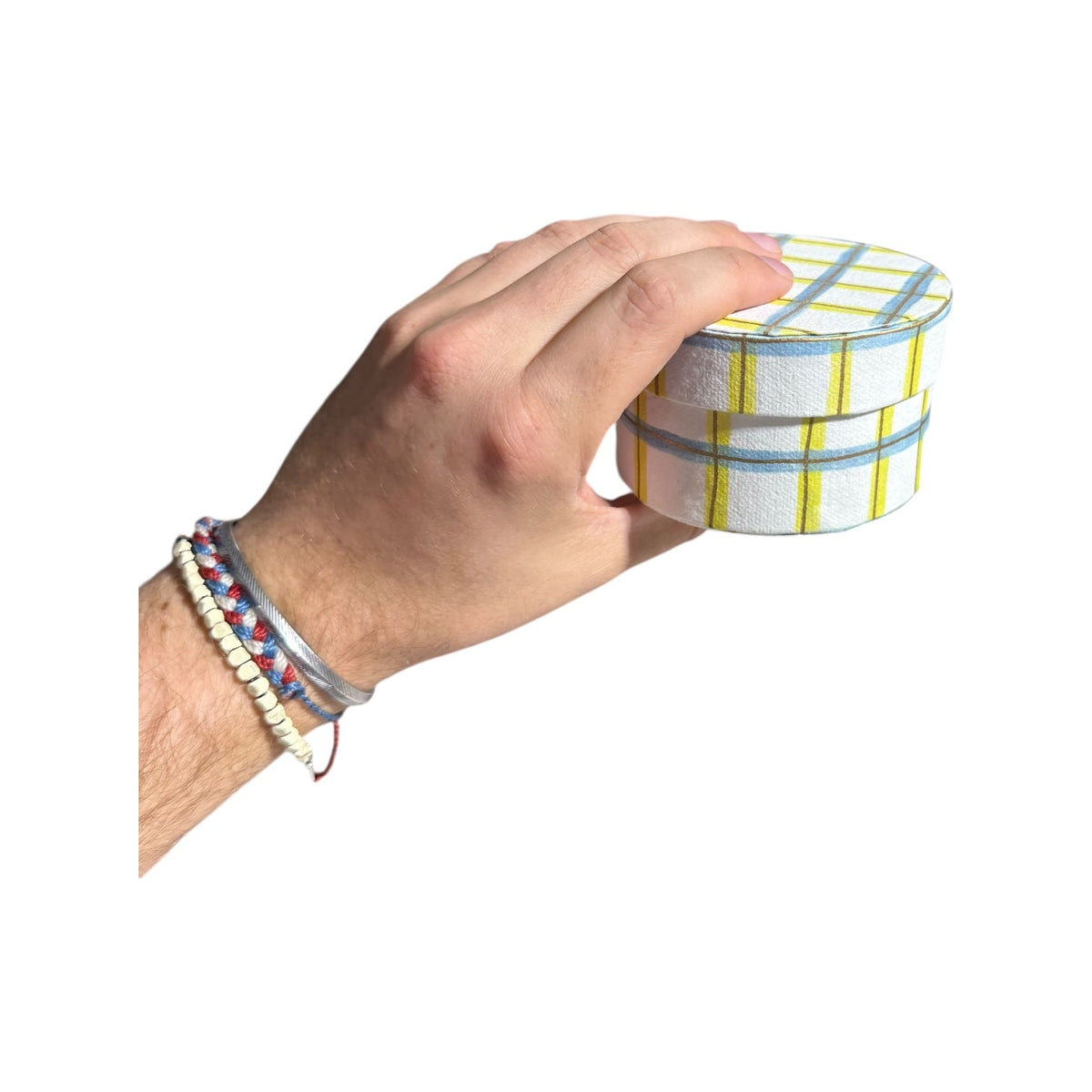 Hand holding a round handmade recycled paper gift box with light blue and yellow plaid stripes.