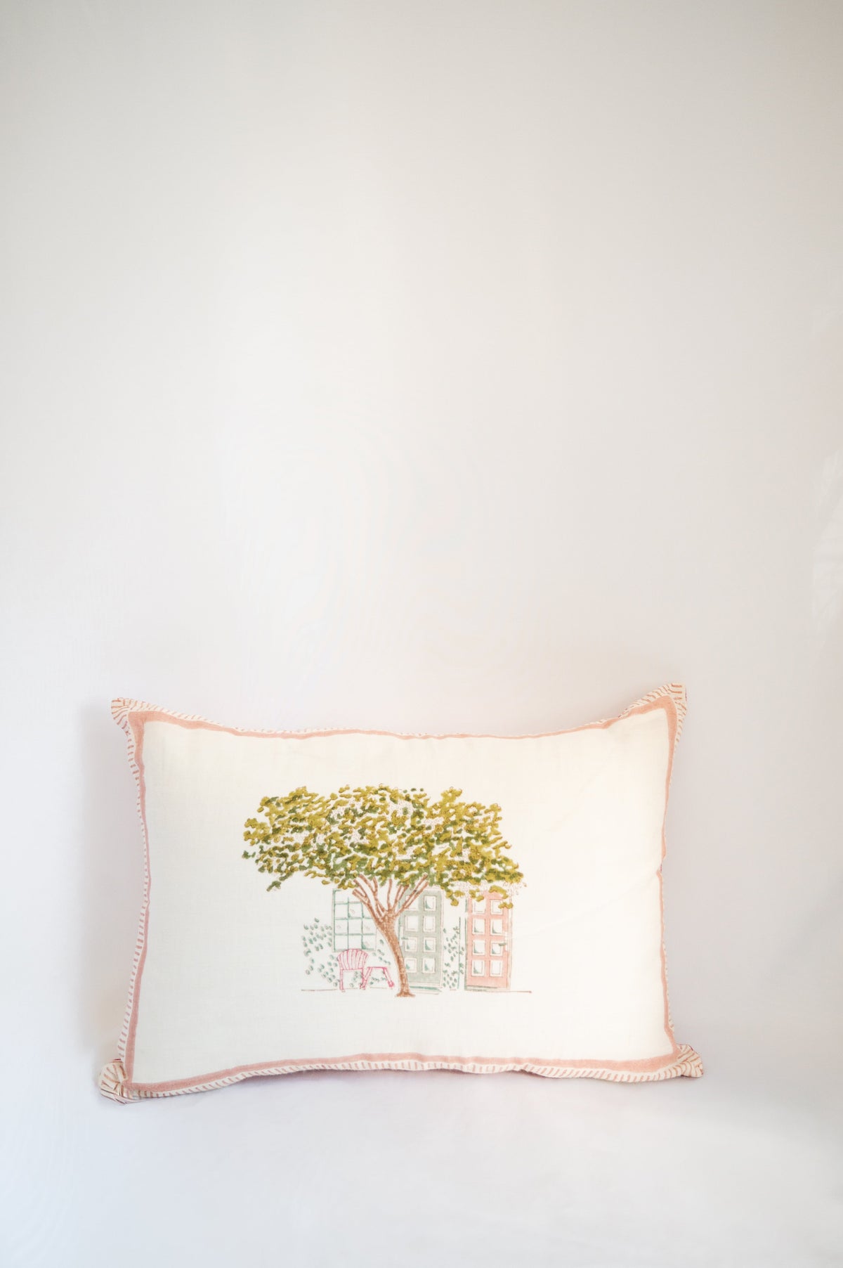 Block print cushion front with yellow tree and house illustration, pink stitched border