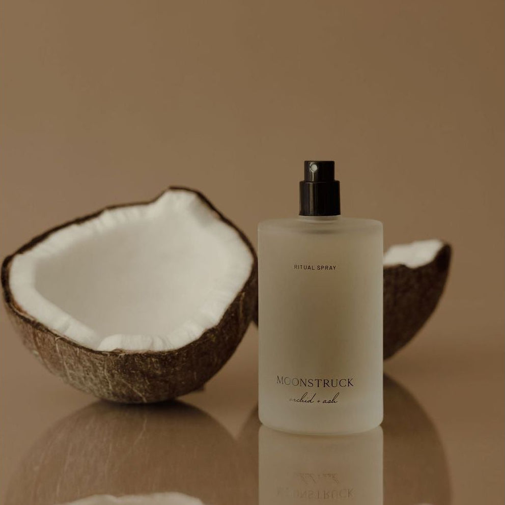 MOONSTRUCK ritual spray bottle with black pump beside halved coconut shell.