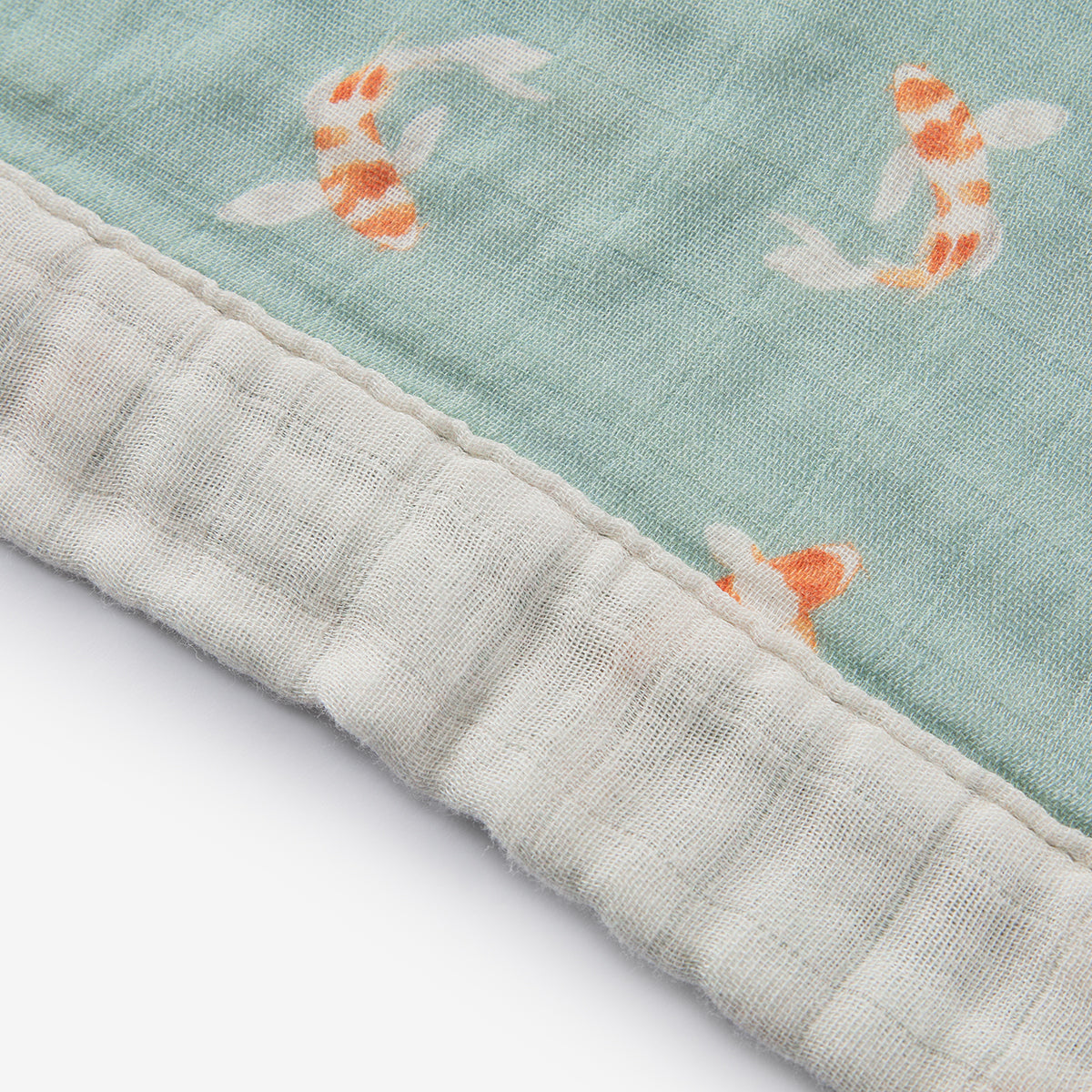 Teal lovey blanket edge with off-white stitched border and orange koi fish pattern