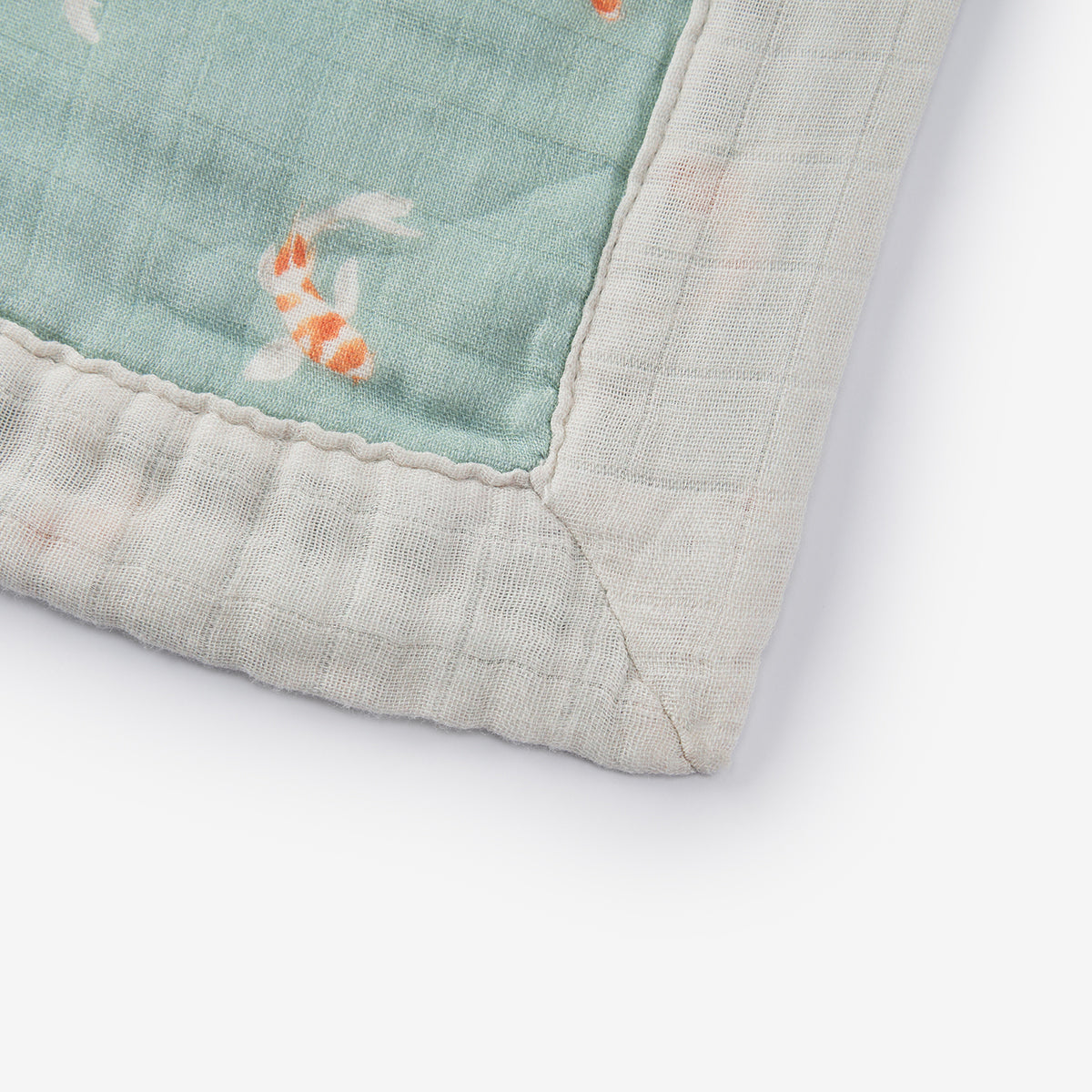 Corner view of teal koi fish lovey blanket with off-white fringed trim