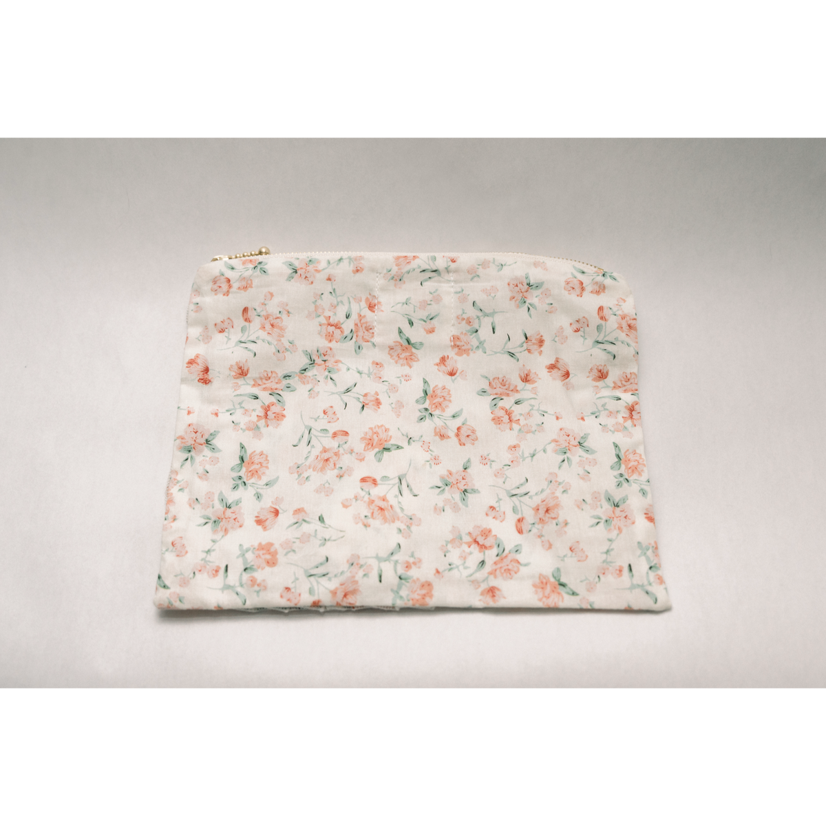 Floral zipper pouch with pastel rose and greenery print on light fabric, ruffled bottom edge
