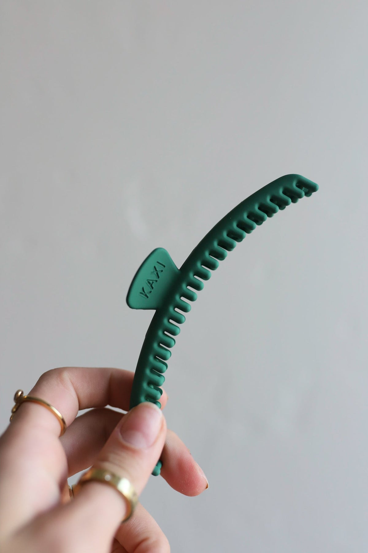 Teal green hair claw clip held in hand with KAXI logo