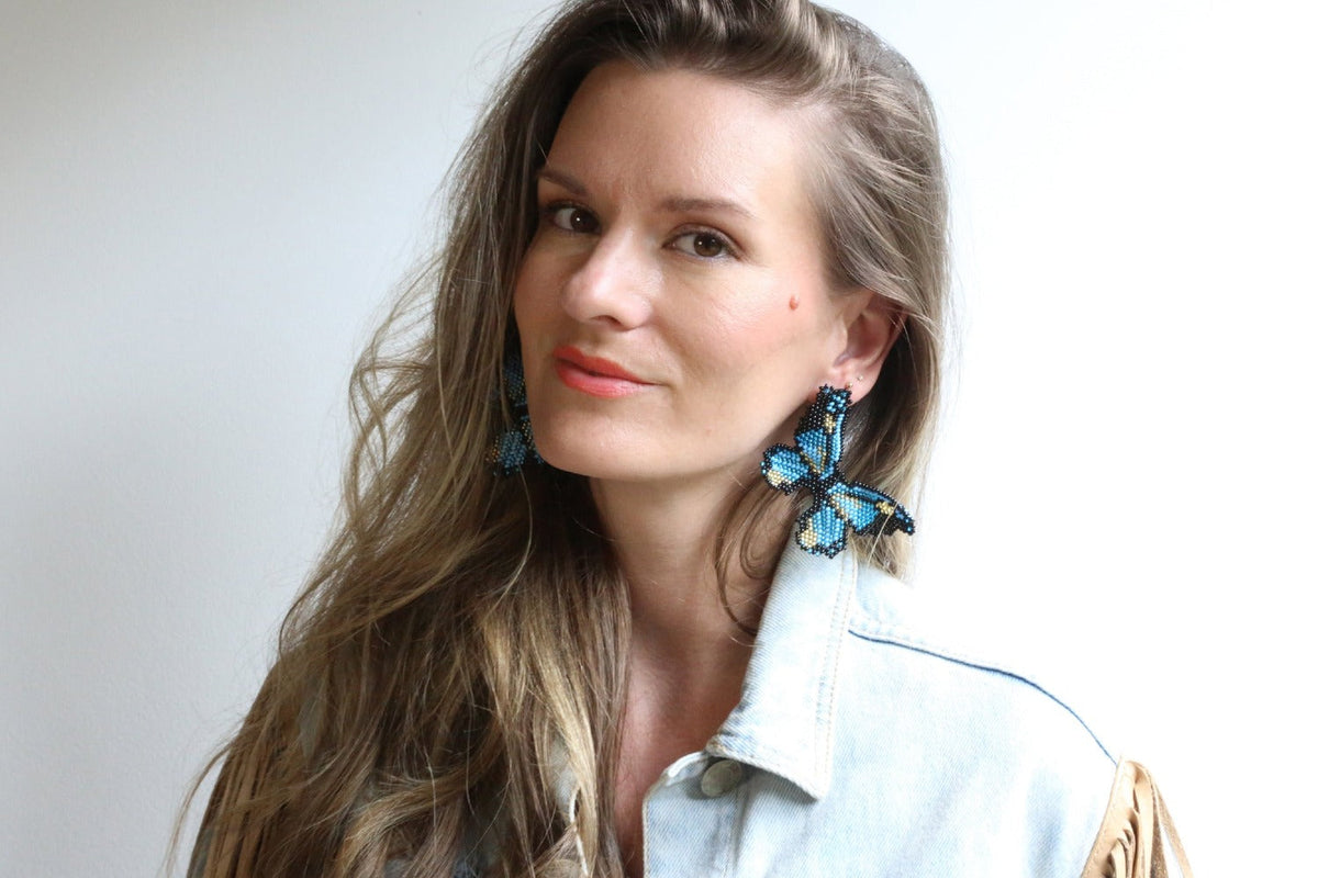 Beaded butterfly earring in blue with black details and gold center, worn