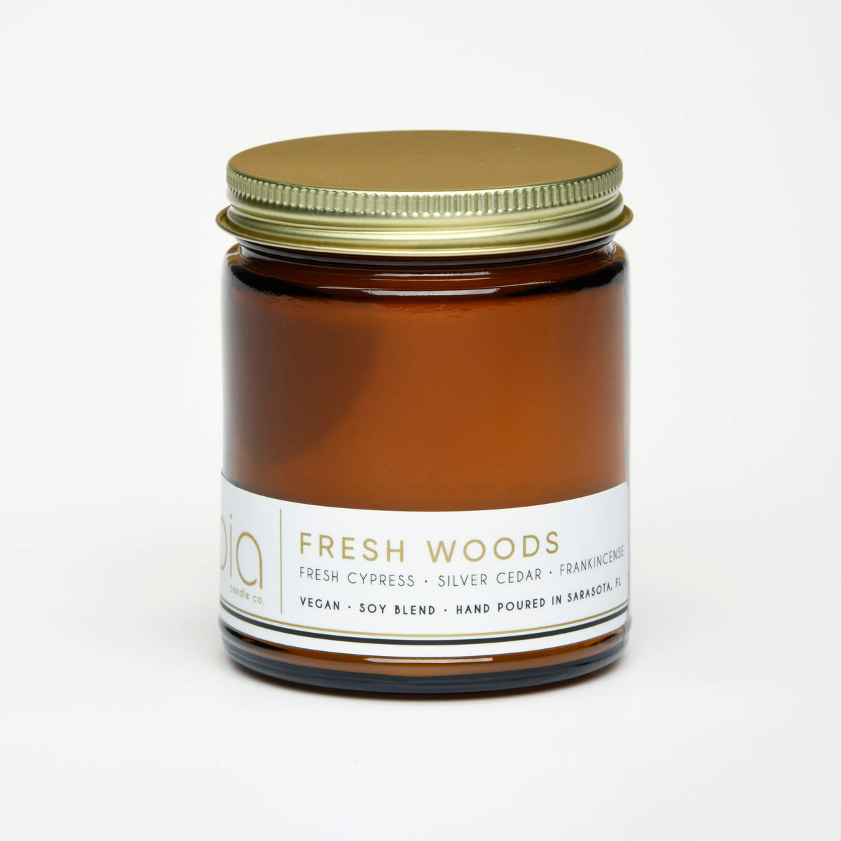 Amber glass candle jar with a gold lid and a white front label with product details.