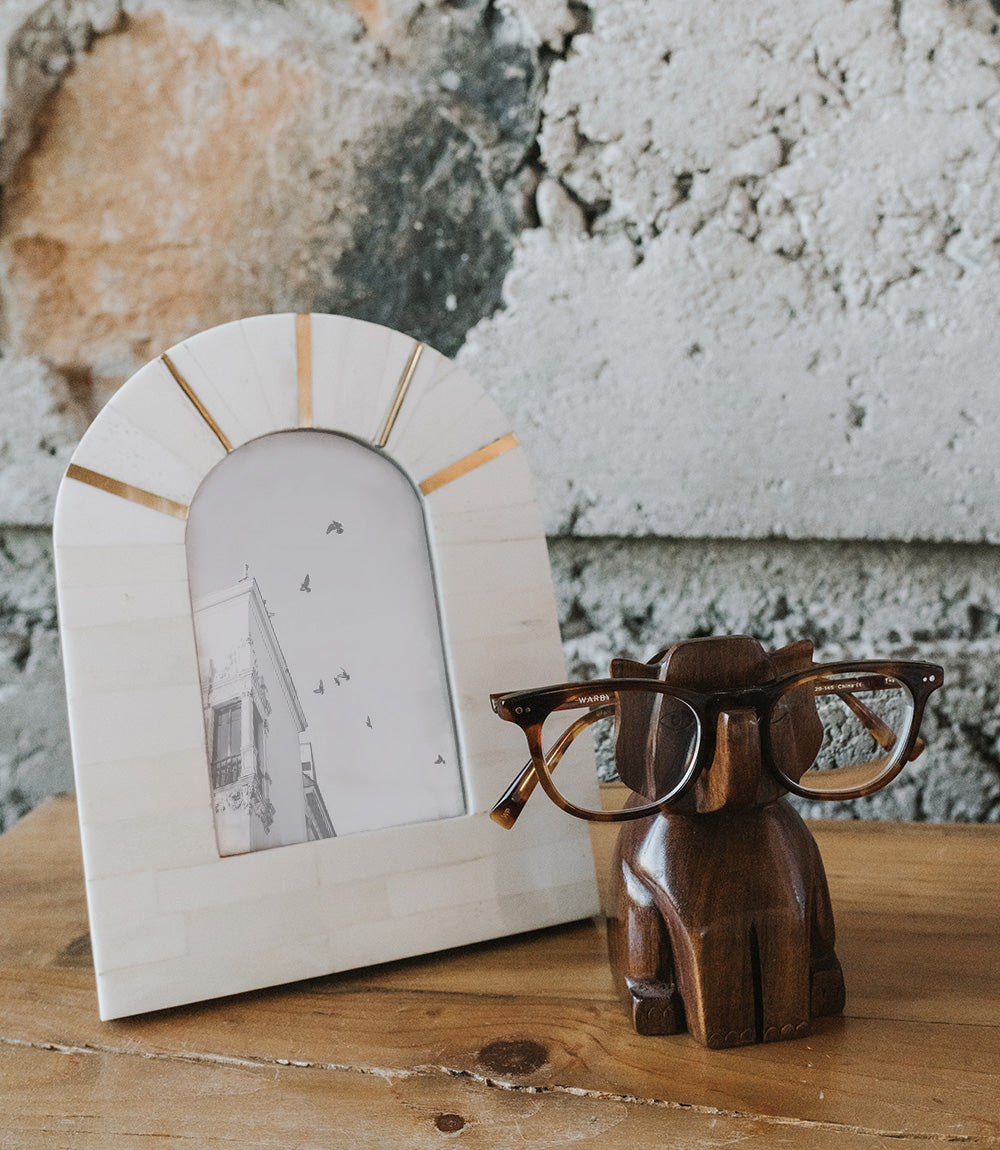Brown wooden elephant eyeglass stand with eyeglasses resting on the top holder.