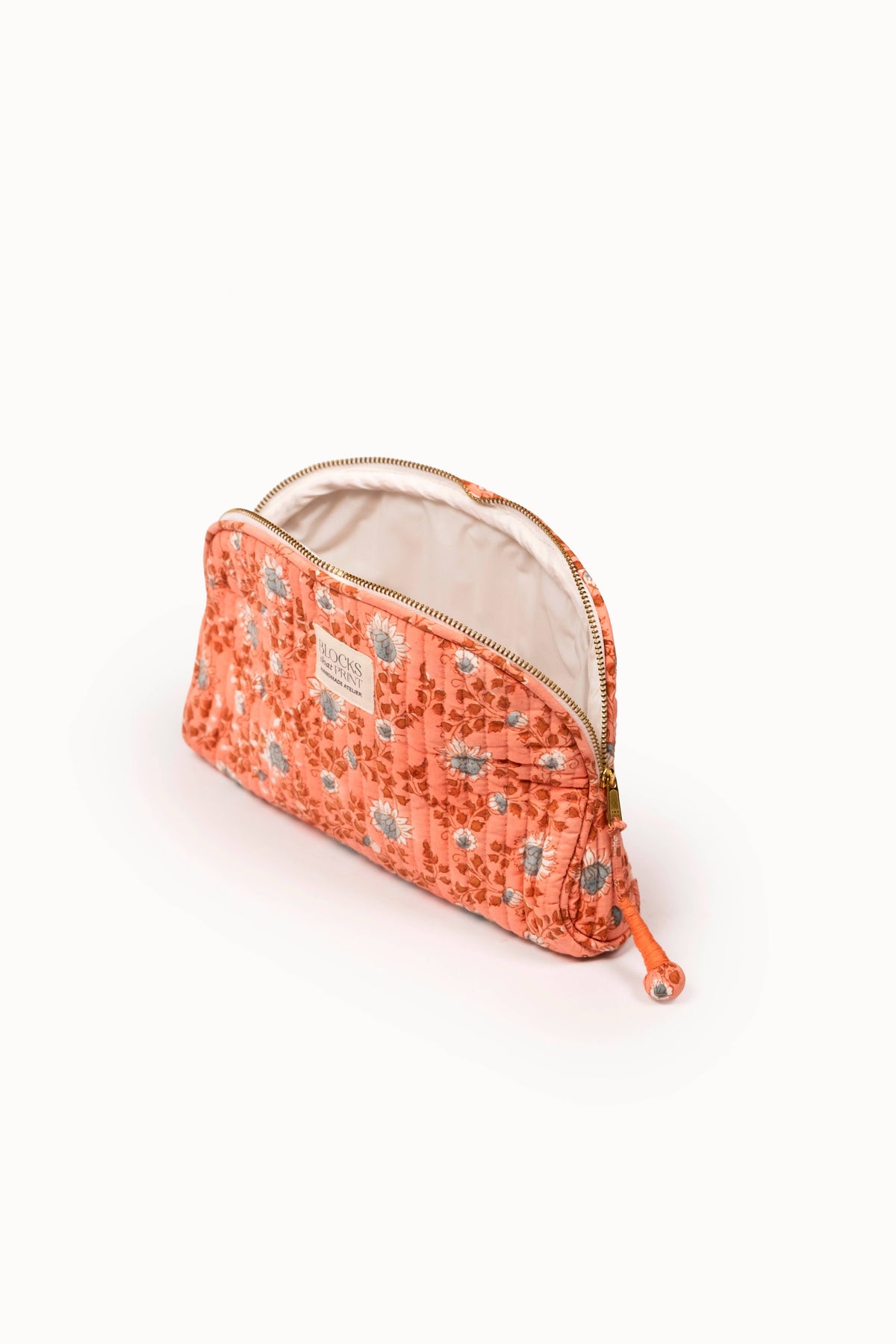 Terracotta quilted travel pouch with tan lining, zip closure, and tassel cord