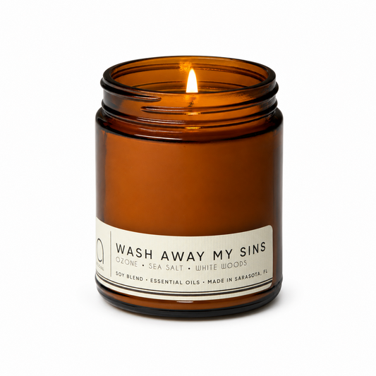 Amber candle jar with lit flame and label text "Wash Away My Sins"