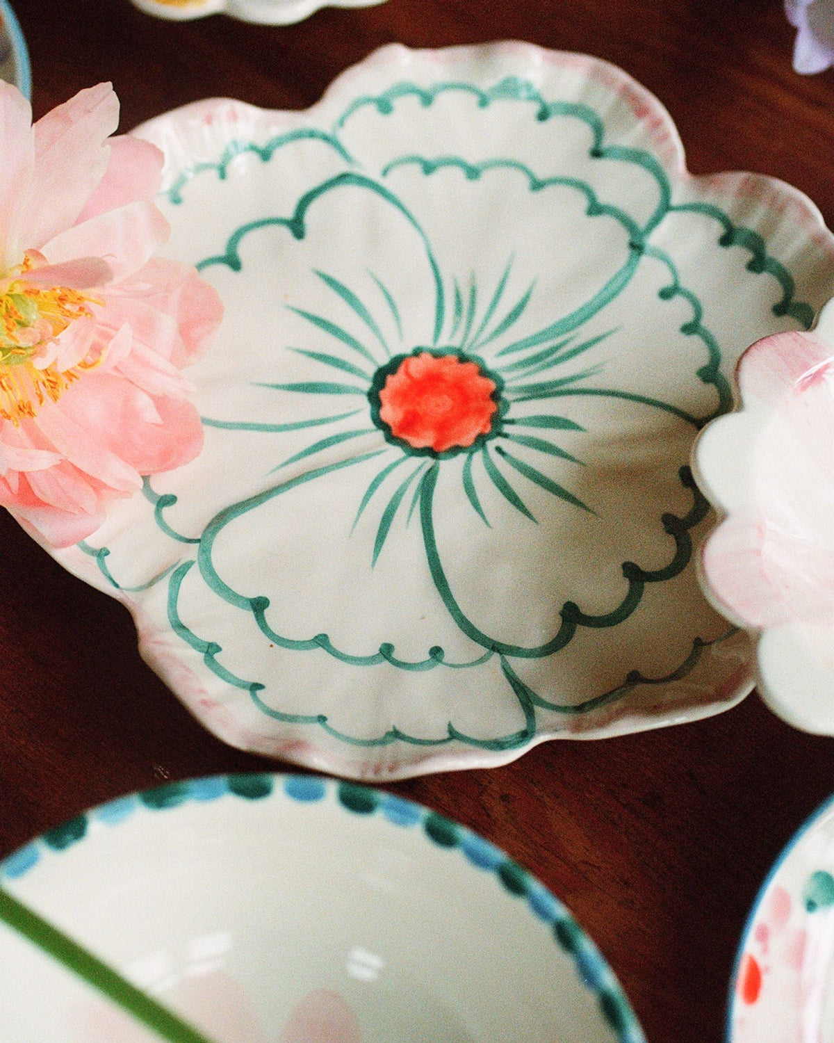 Ceramic flower-shaped side plate with pink scalloped edge, green border and orange flower