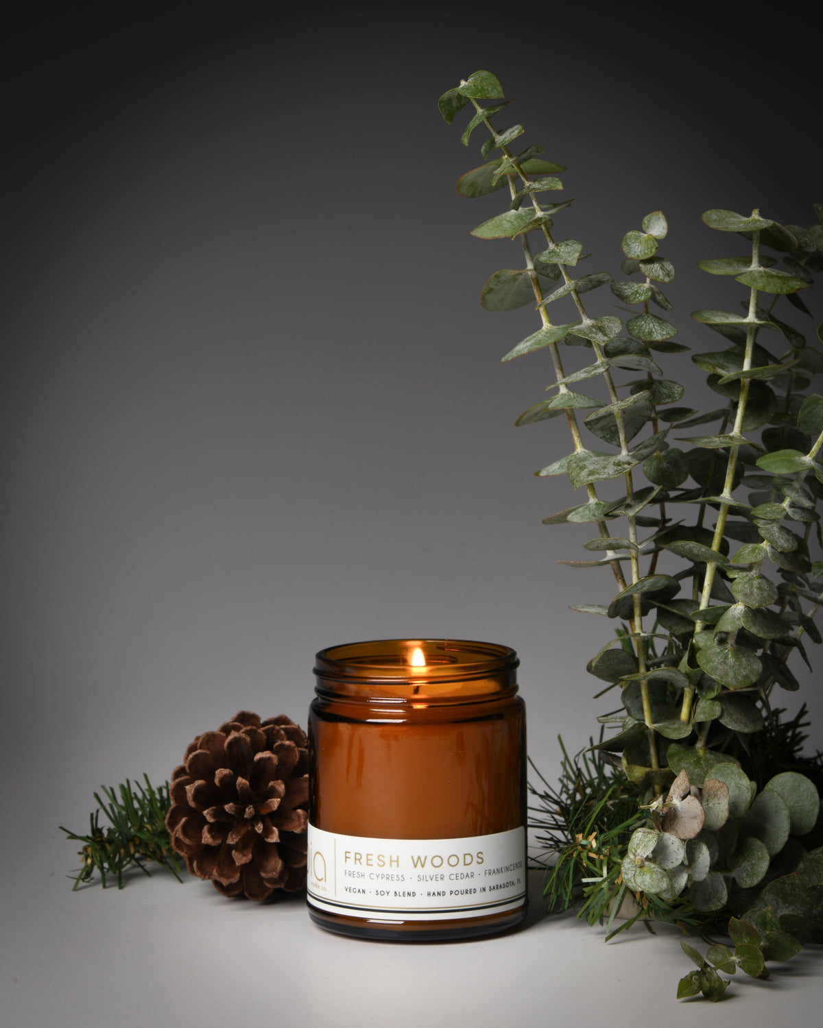 Amber glass candle jar with a single flame, white label visible on the front.