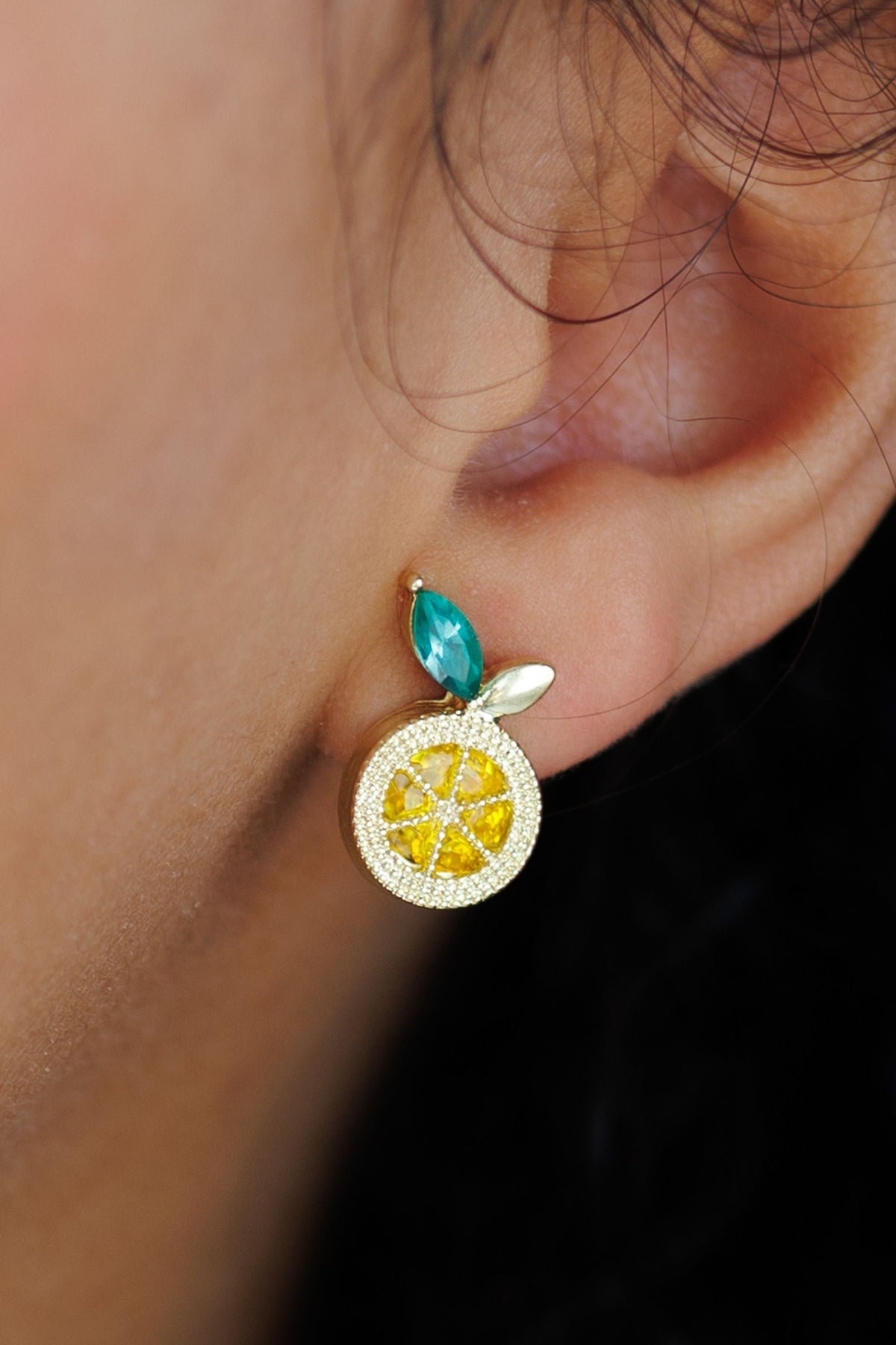 Lemon stud earring with gold textured round charm, teal top, and green leaf detail on ear