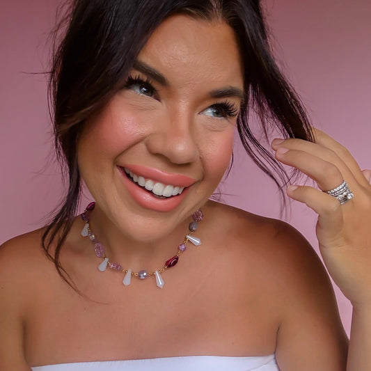 Lavender crystal necklace with small heart charms on a woman, gold-tone chain visible