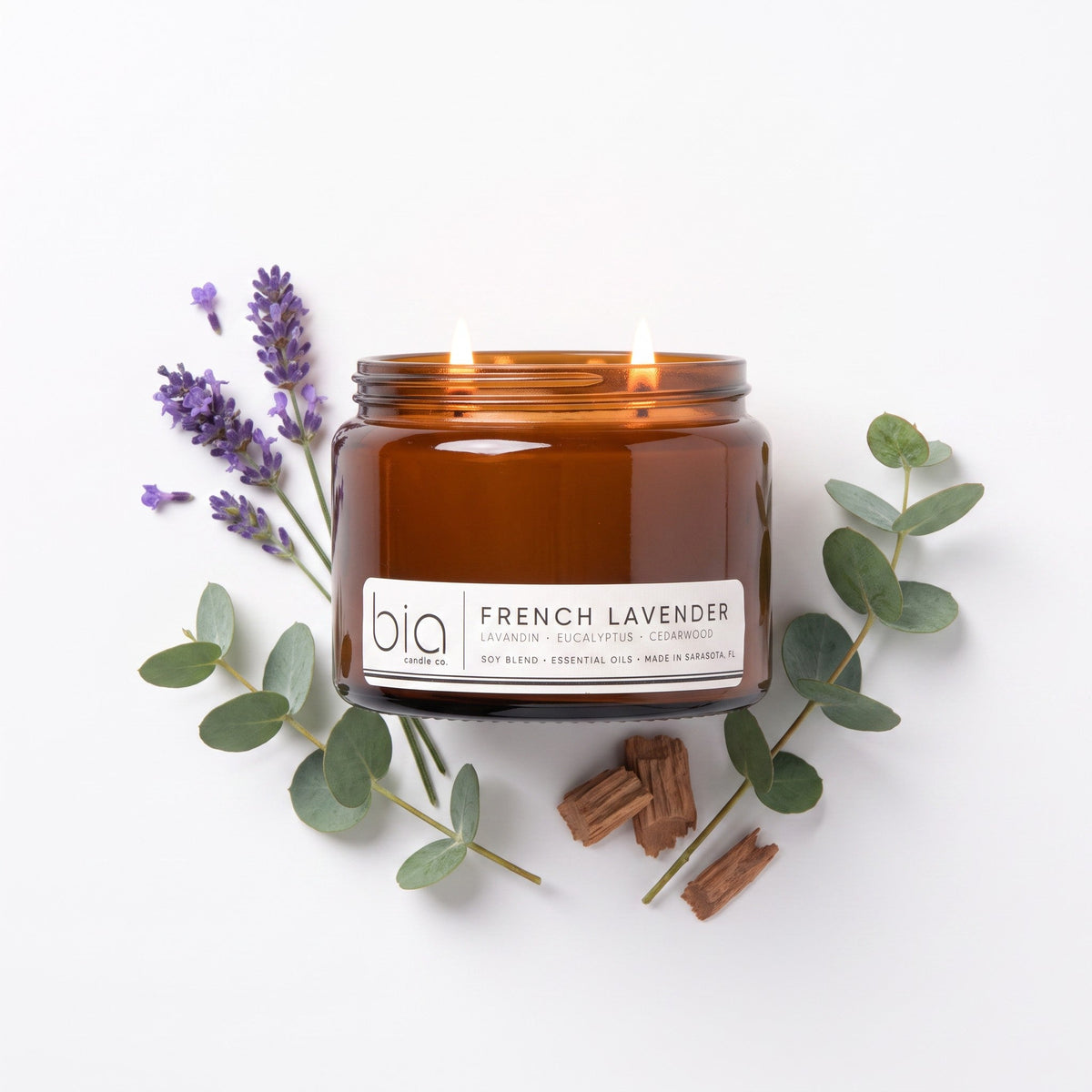 Amber soy candle jar with lit flame, French Lavender label, lavender sprigs and eucalyptus leaves