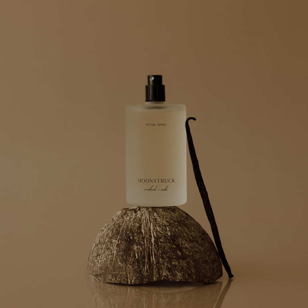 MOONSTRUCK ritual spray bottle with black pump, next to coconut half and vanilla pod