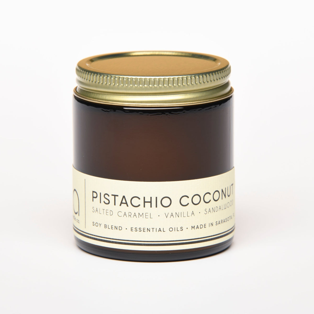 Amber glass candle jar with gold lid and white label reading Pistachio Coconut