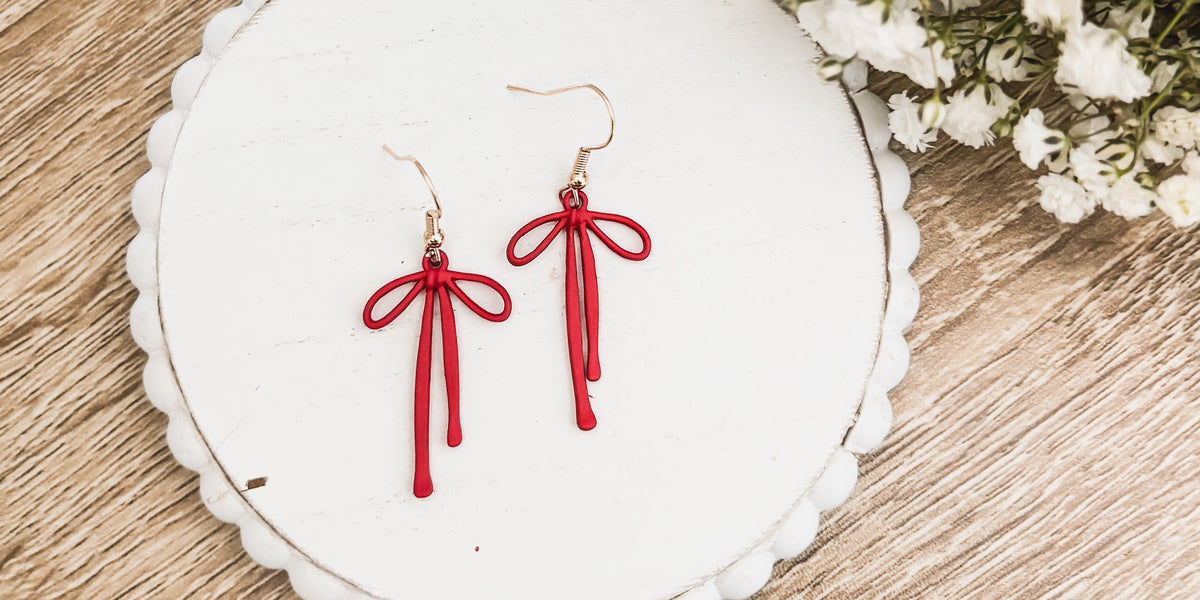 Red bow drop earrings with dangling tassels and gold-tone hooks on a white round card