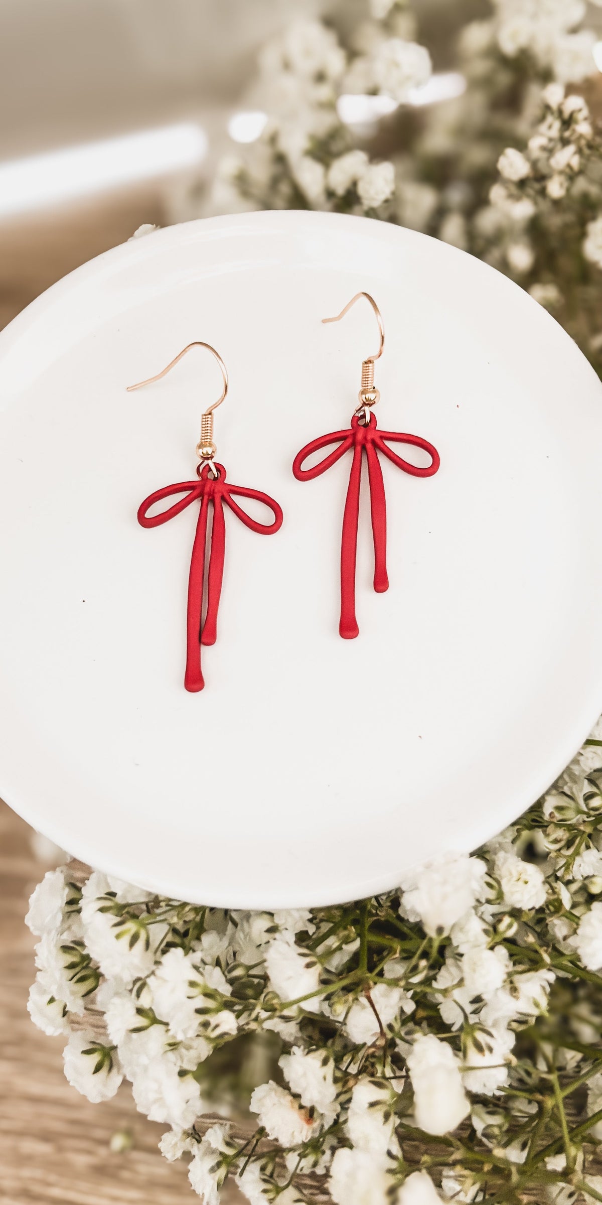 Red bow drop earrings with tassel drops and gold-tone hooks on a white display plate