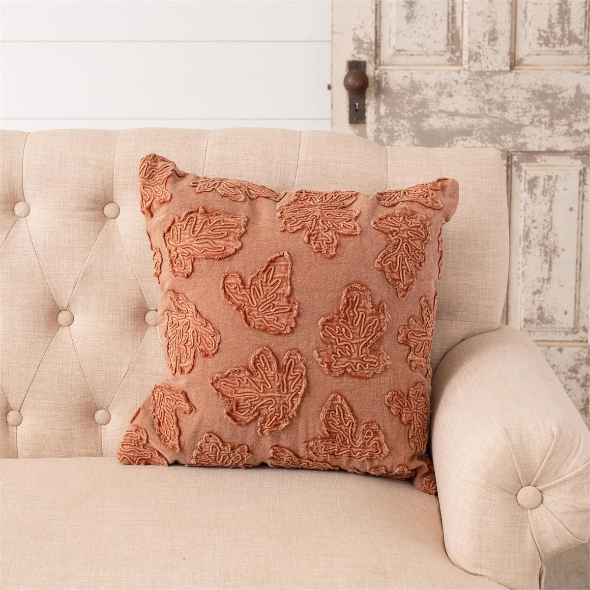 Square throw pillow featuring rust-orange embroidered leaf motifs