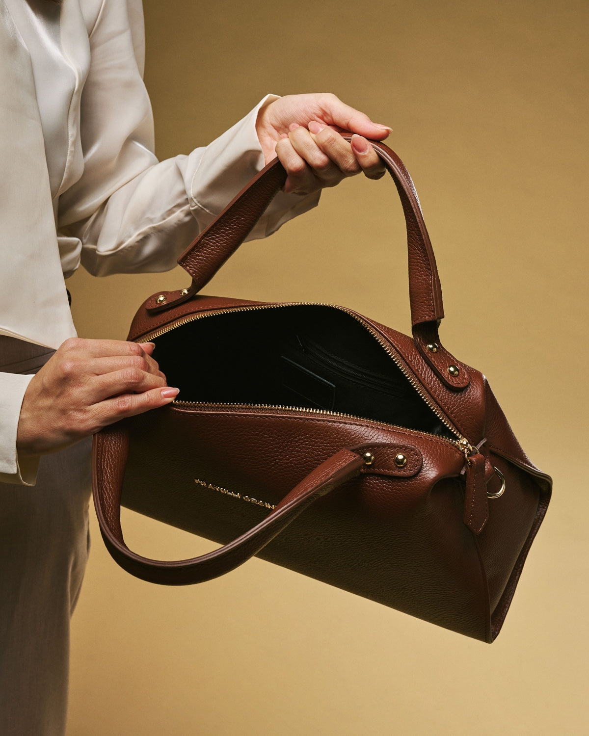 Brown leather handbag with open zip-top and gold zipper trim, side pocket detail