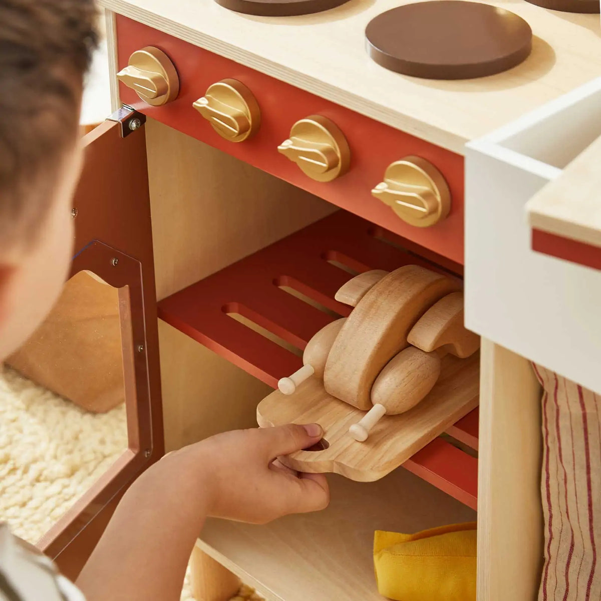 Wooden play kitchen oven opened to show a removable wooden tray and play food