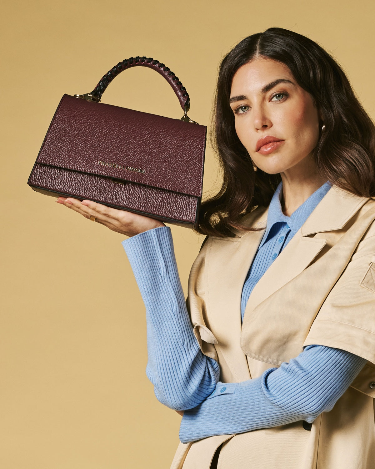 Eggplant leather crossbody bag held in hand, textured finish and top flap