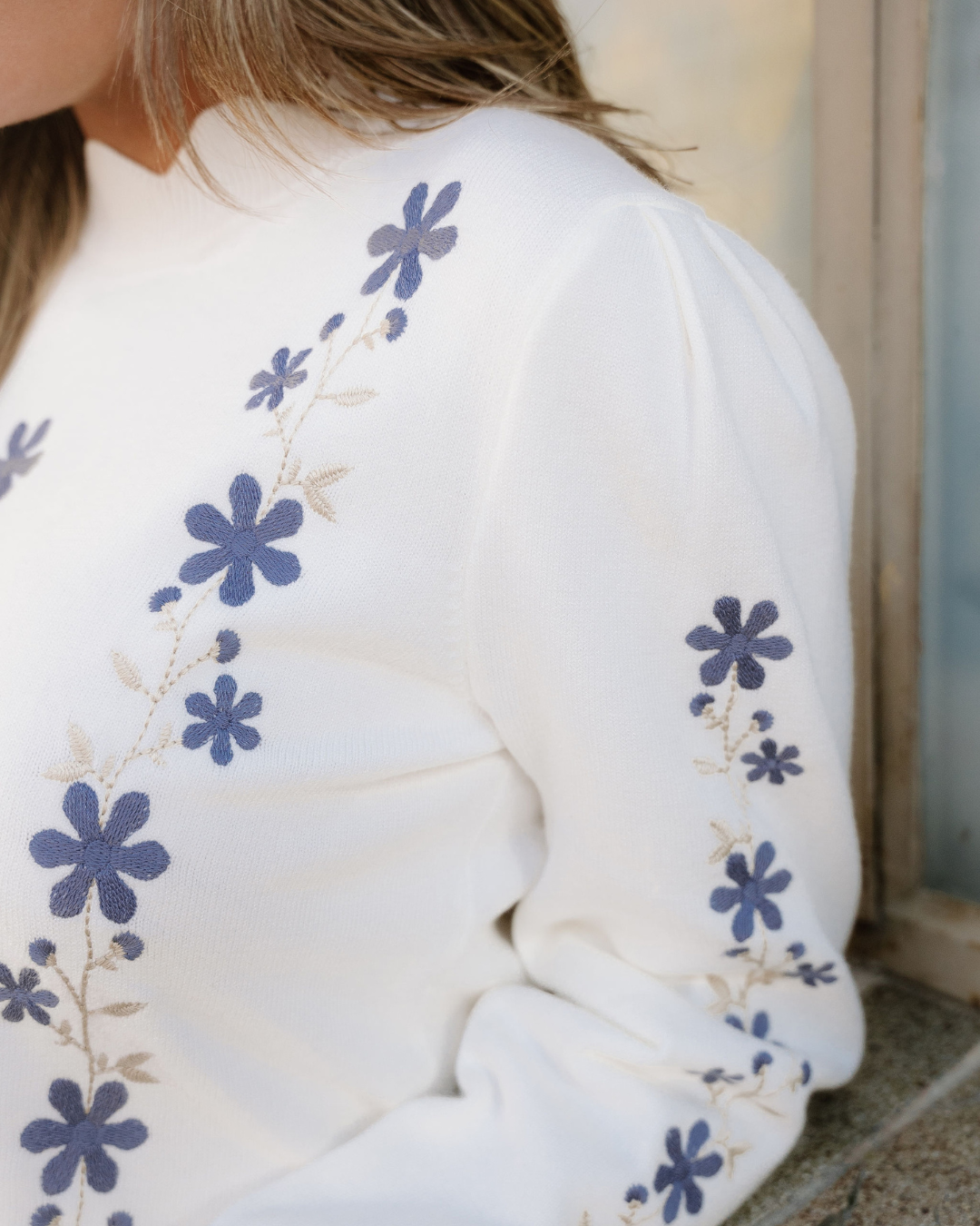 Close-up of white sweater sleeve with blue floral embroidery
