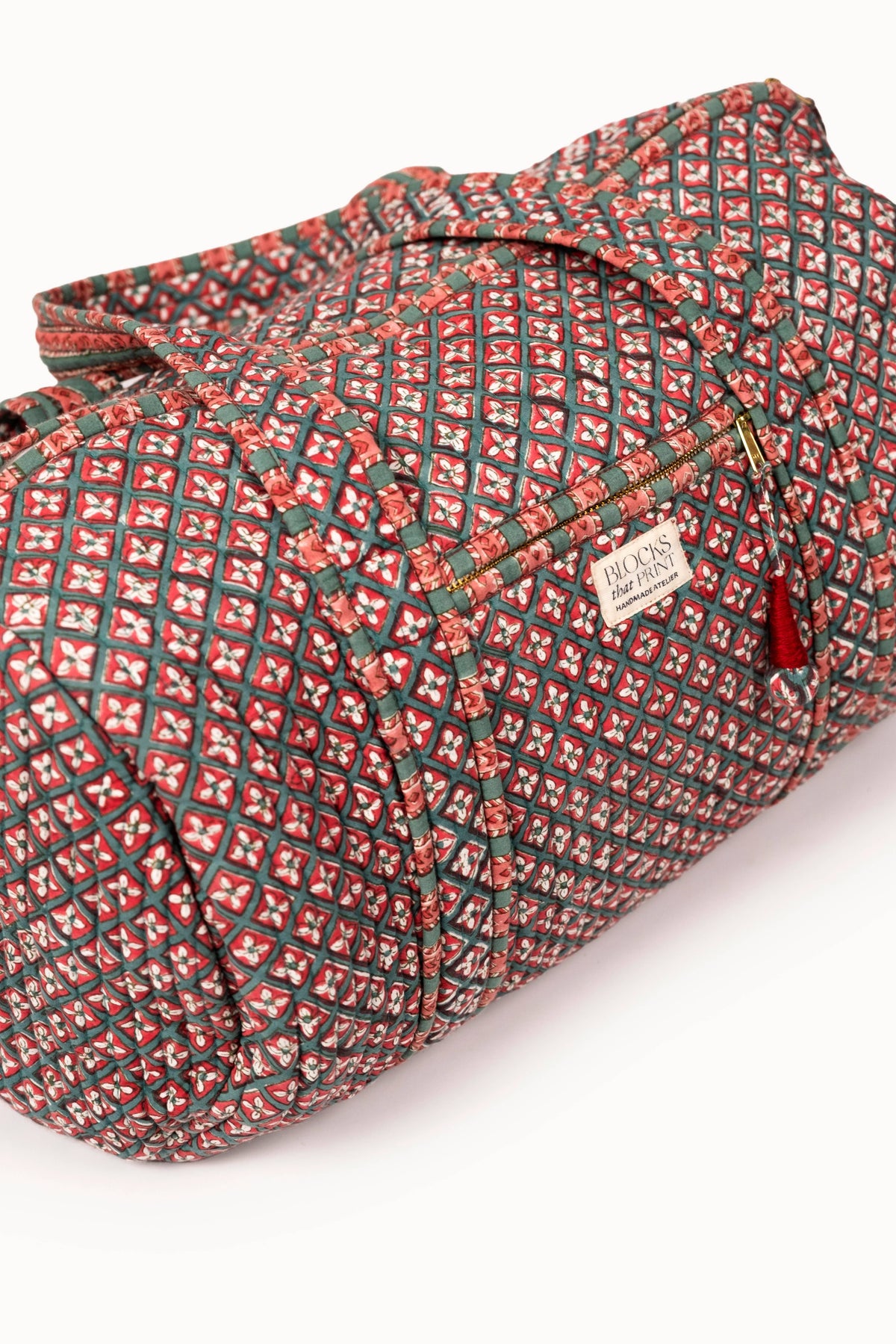 Quilted duffle bag with red-and-green geometric print, green handles, front label patch
