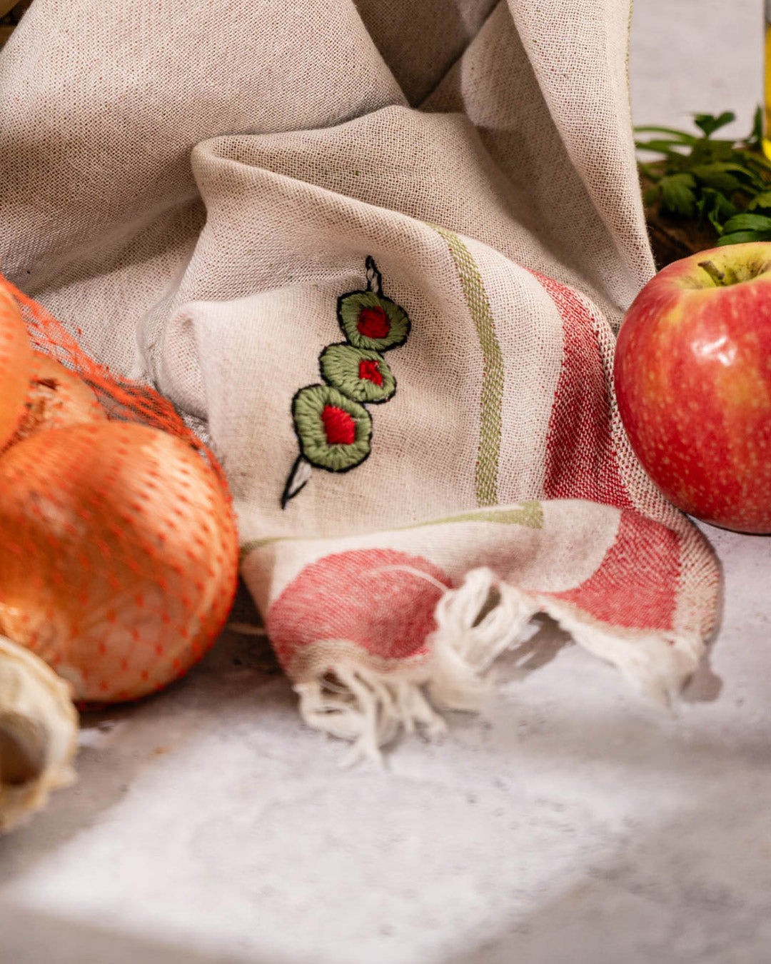 Kitchen towel close-up: cream with red stripe edge, green olive embroidery, fringed hem