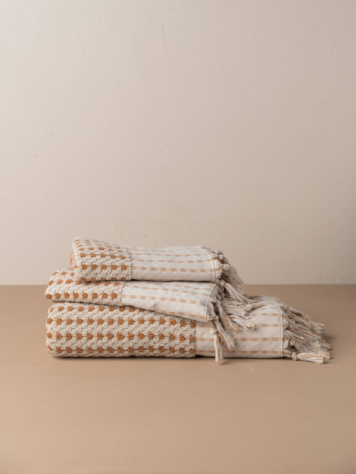 Turkish hand towel stack with terracotta grid, stone stripes, and tasseled fringe