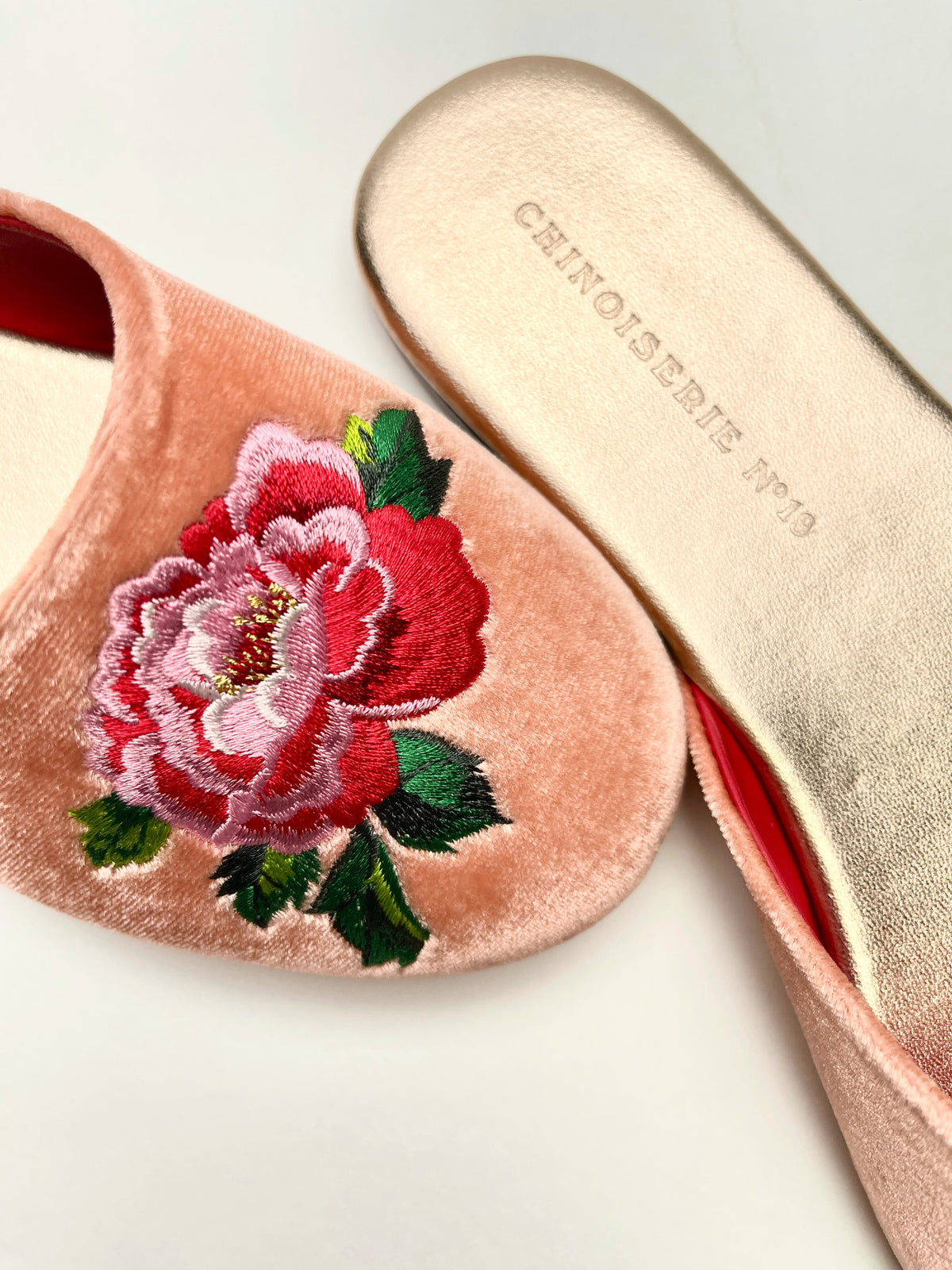 Close-up of peach velvet mules with colorful peony embroidery on the toe