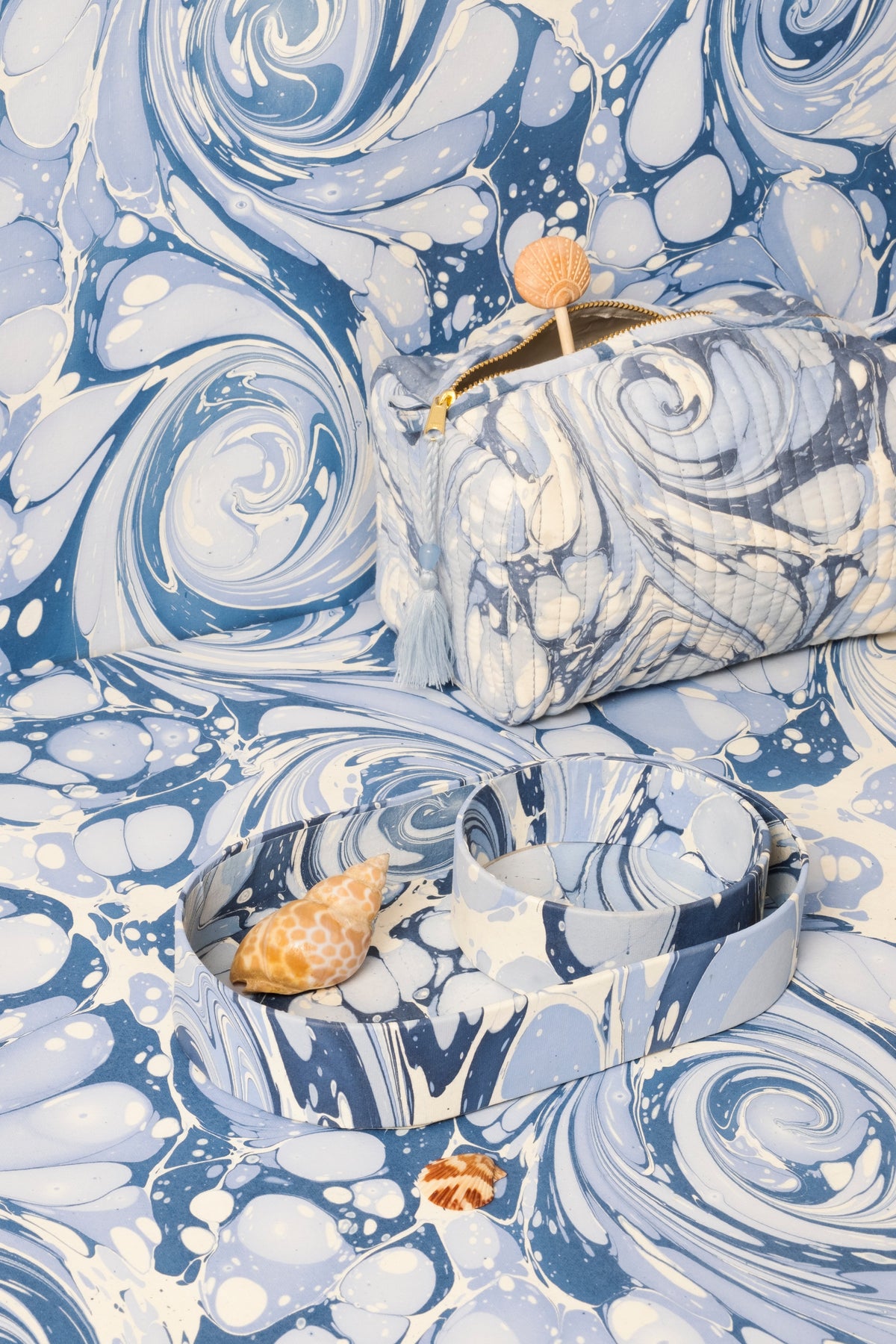 Blue hand-marble cosmetic bag with gold zipper pull and small shell charm on fabric