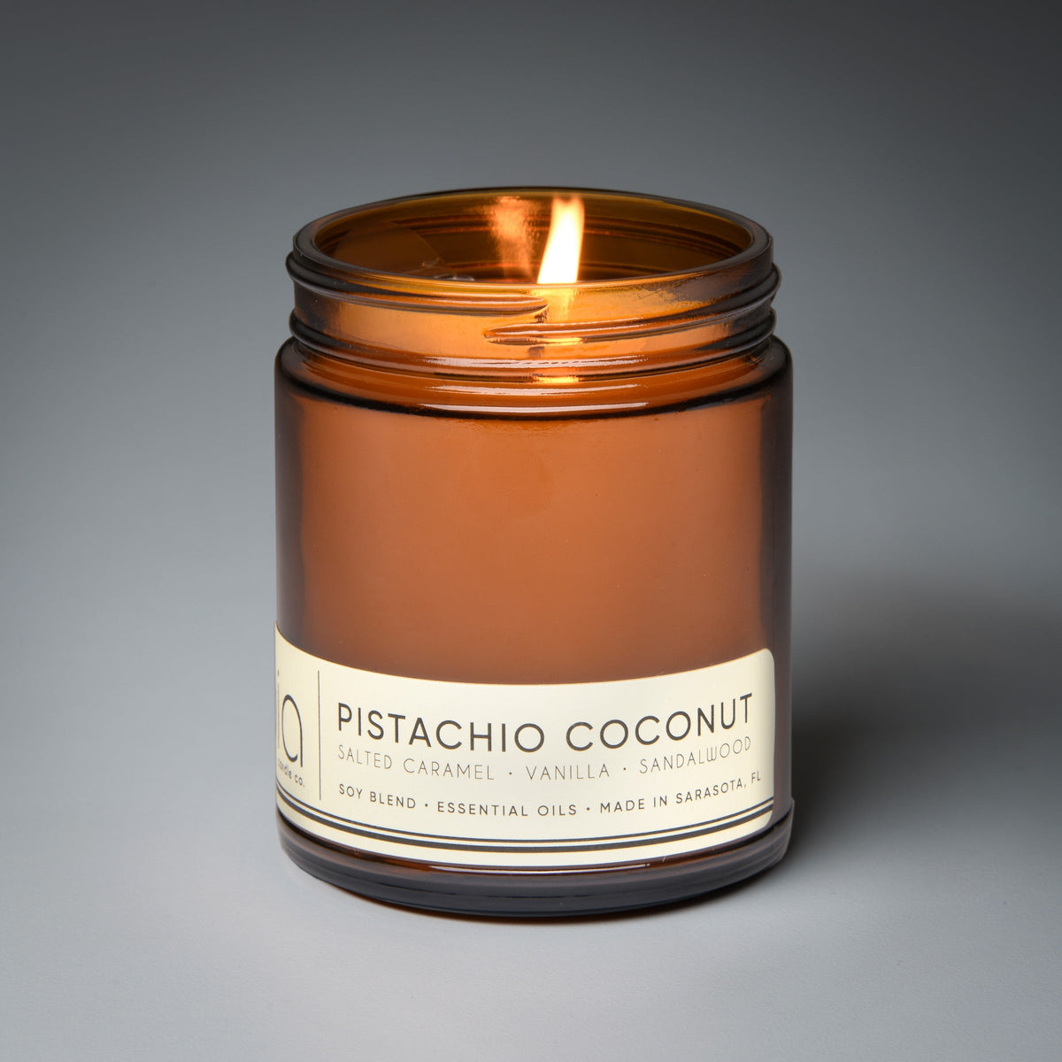 Amber glass candle jar with lit wick and “Pistachio Coconut” label