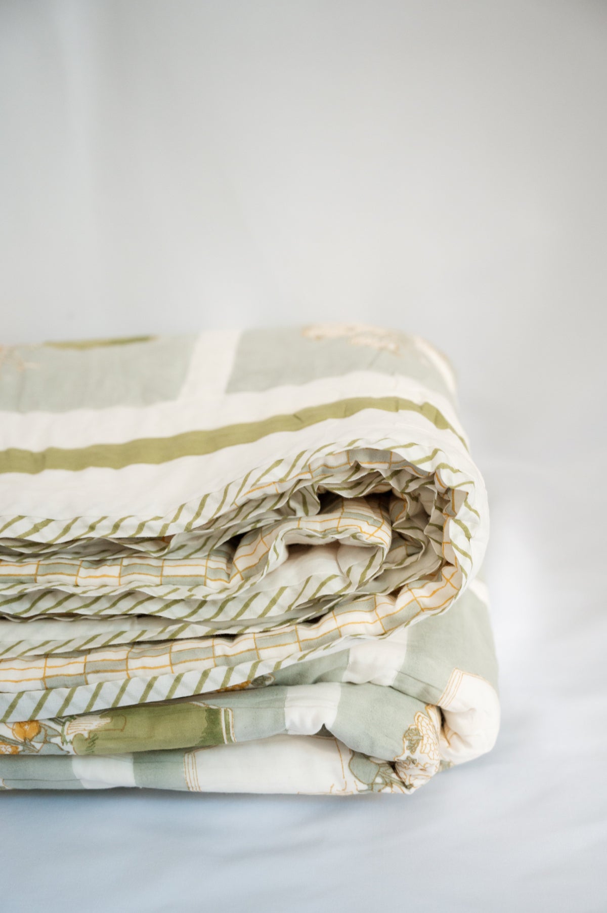 Rolled quilt with green, white, and yellow stripes and layered stitched panels