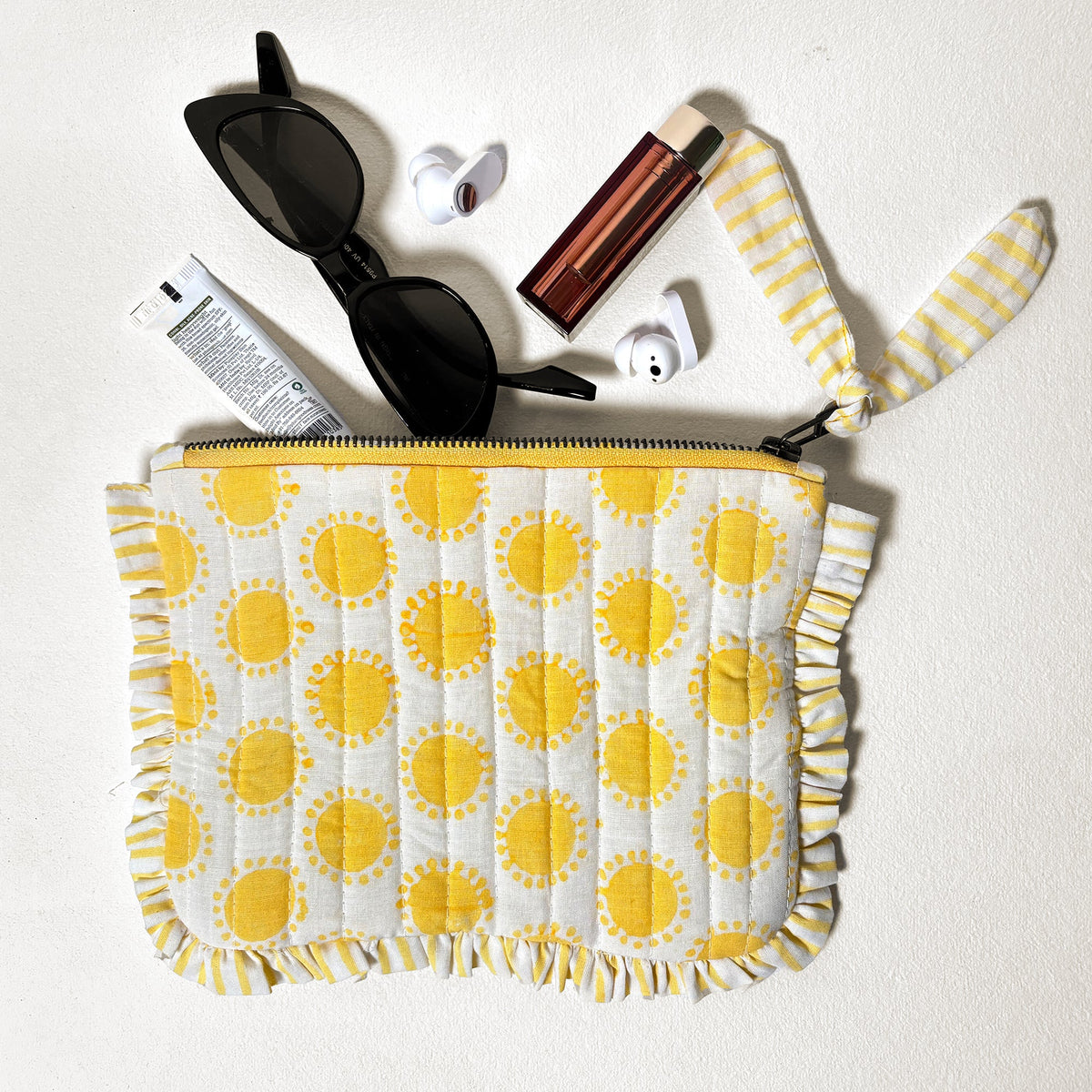 Quilted cotton travel pouch with yellow sun print, ruffle trim, and black zipper closure