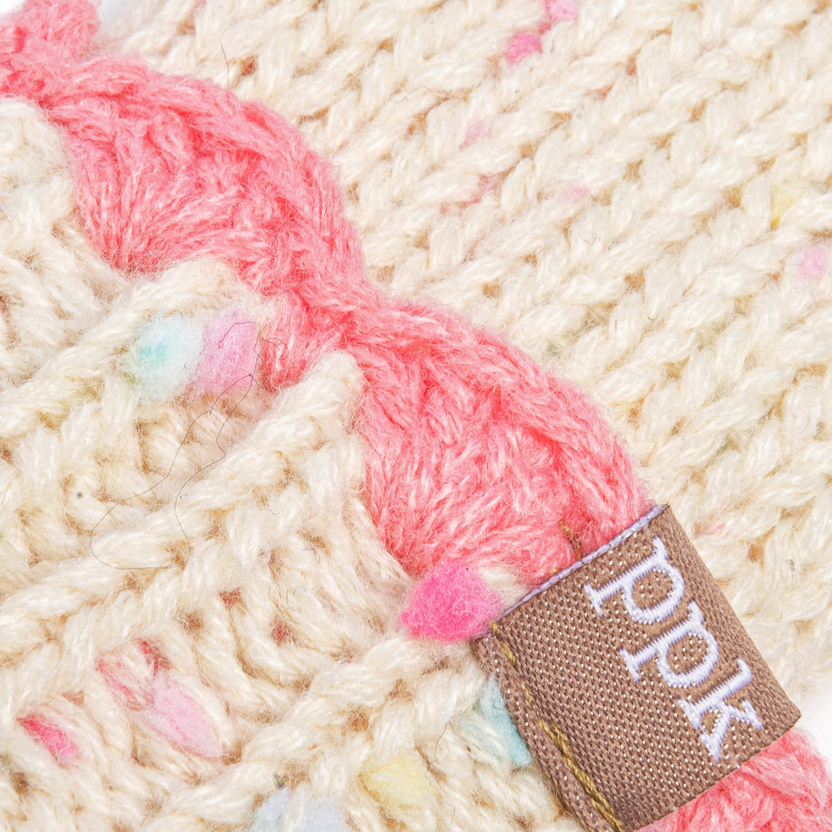 Close-up of cream flecked knit mittens with a pink cuff and small fabric label