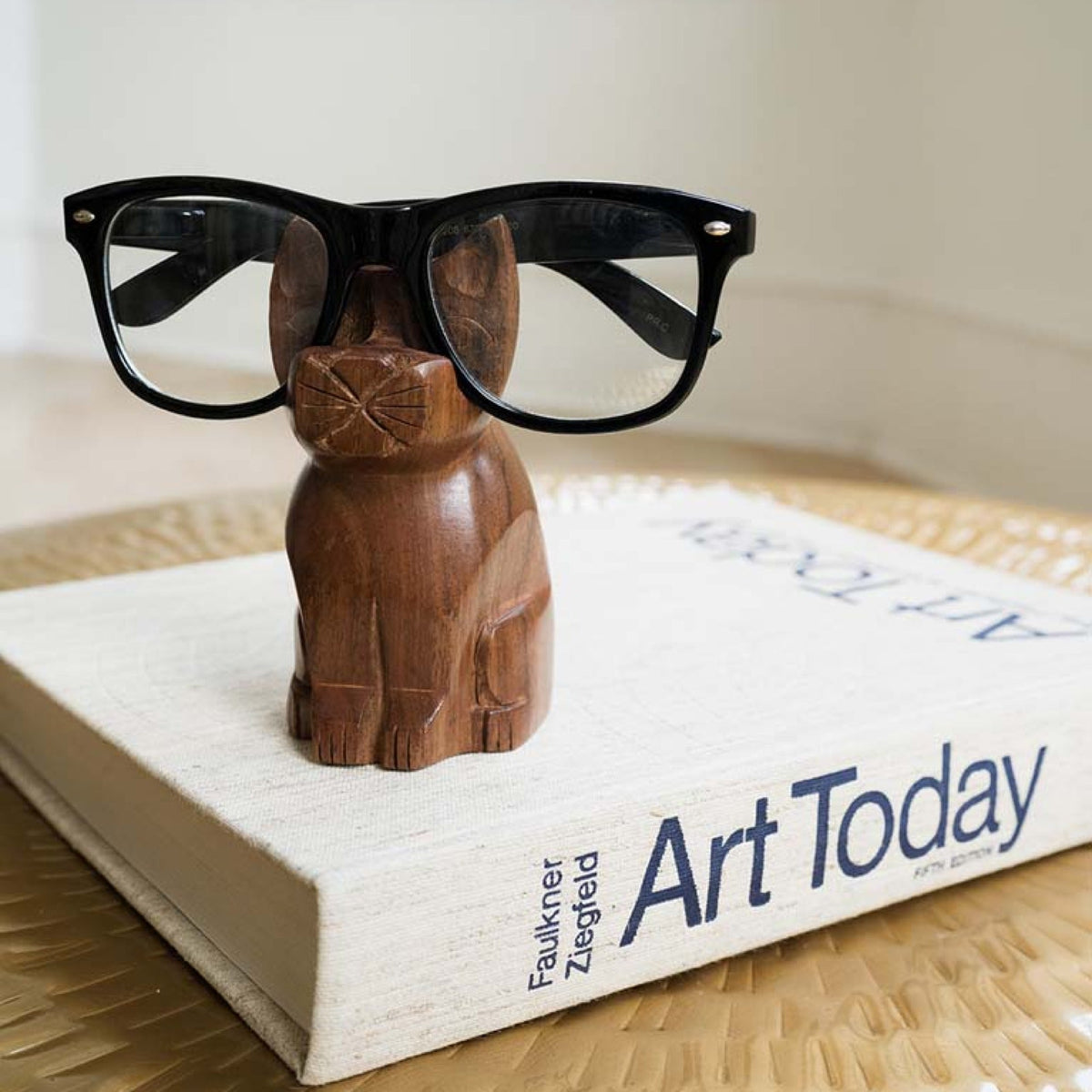 Hand-carved wooden cat eyeglass stand with black eyeglass frames, close angle